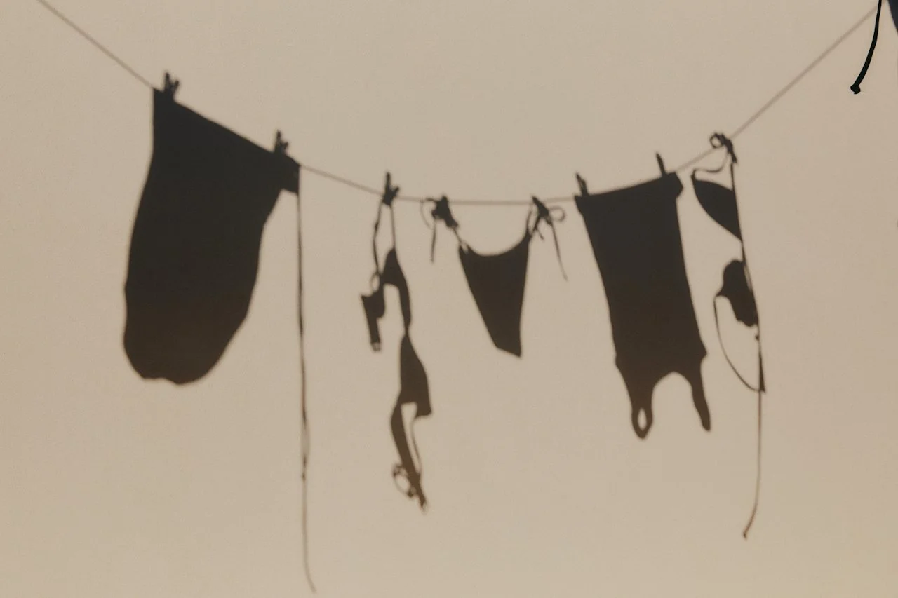 Silhouette of laundry hanging on a clothesline against a plain background.