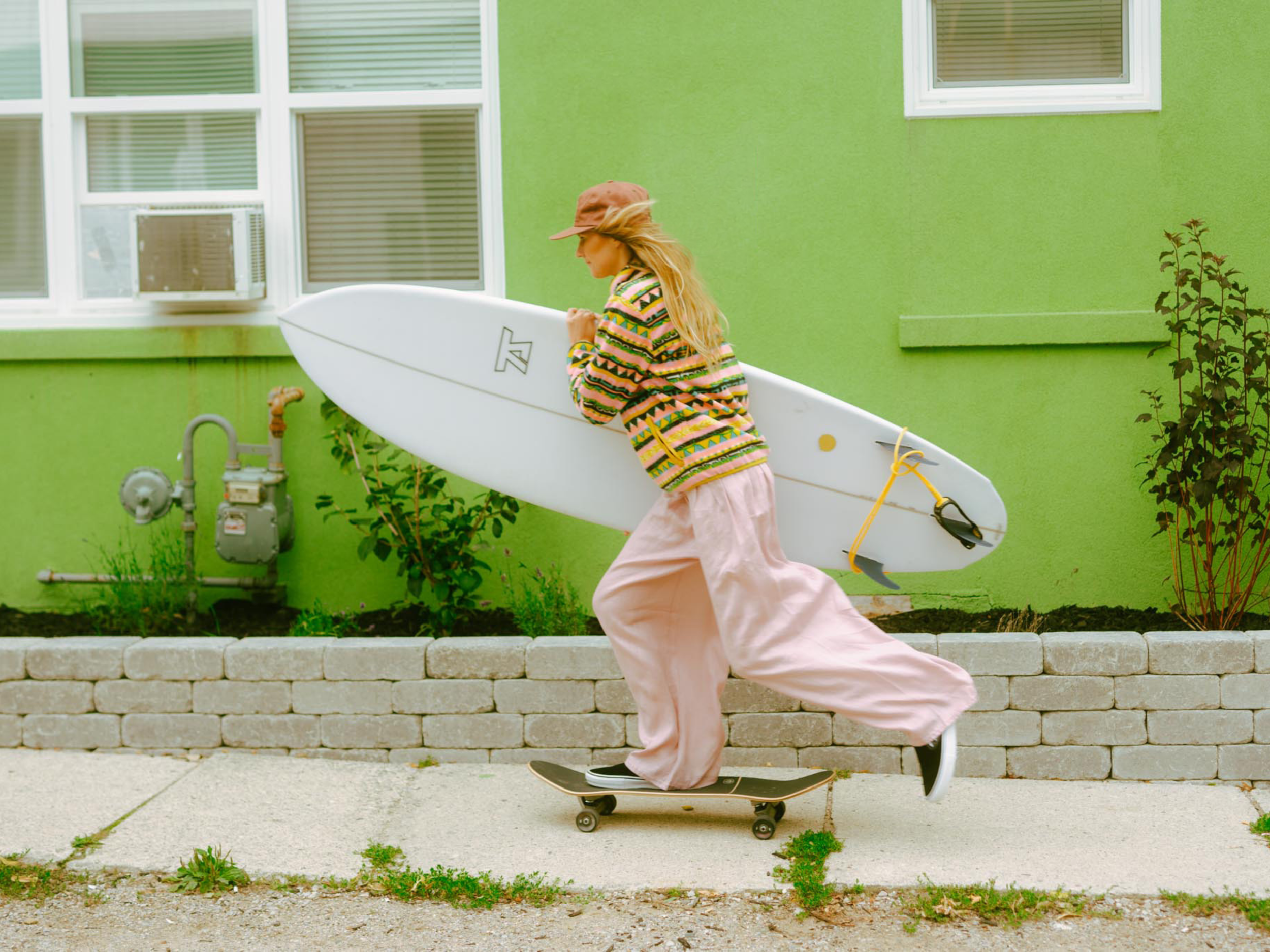 A woman skateboarding on a sidewalk while carrying a surfboard.