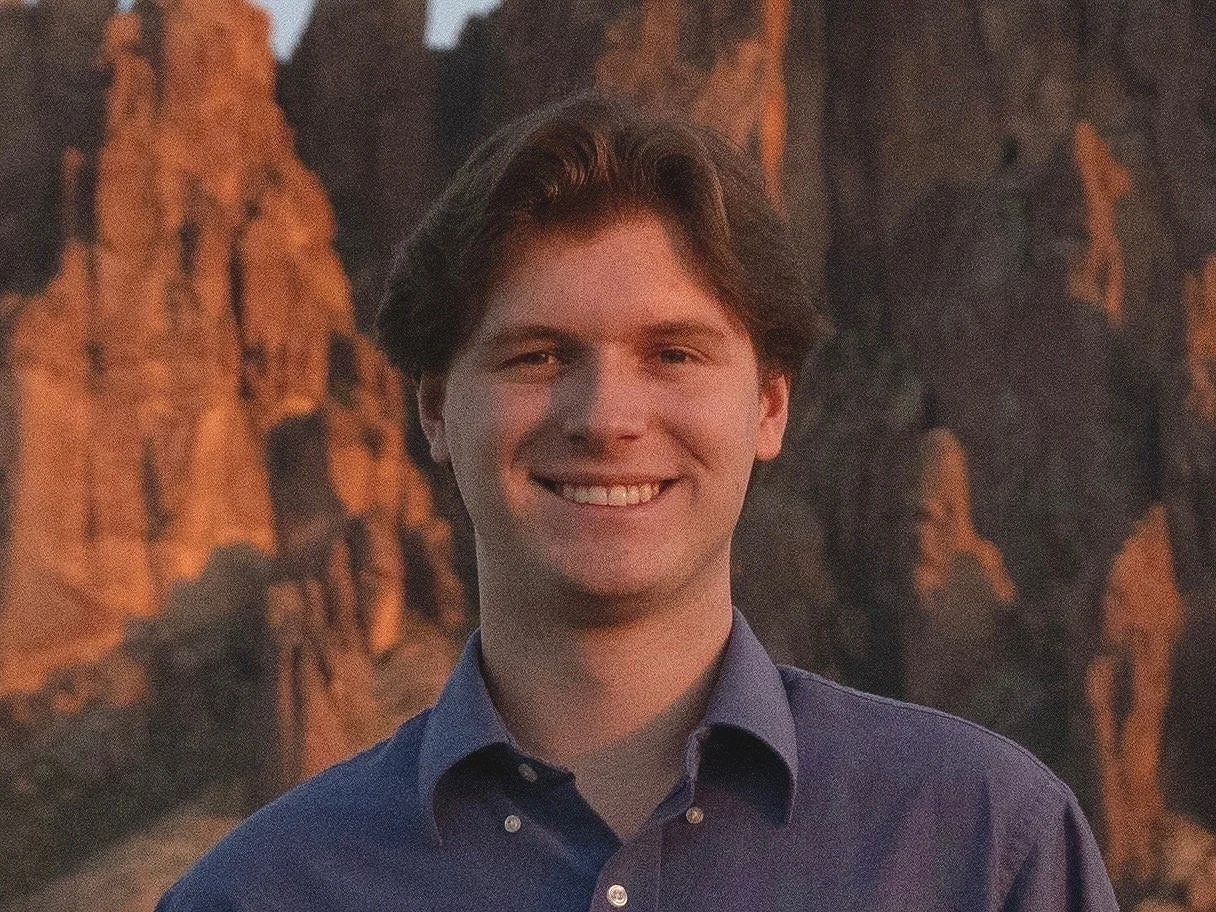 Stryder Bigler, Co-Founder and COO of Off The Record USA, smiling in front of the Superstition Mountains at sunset in Arizona.