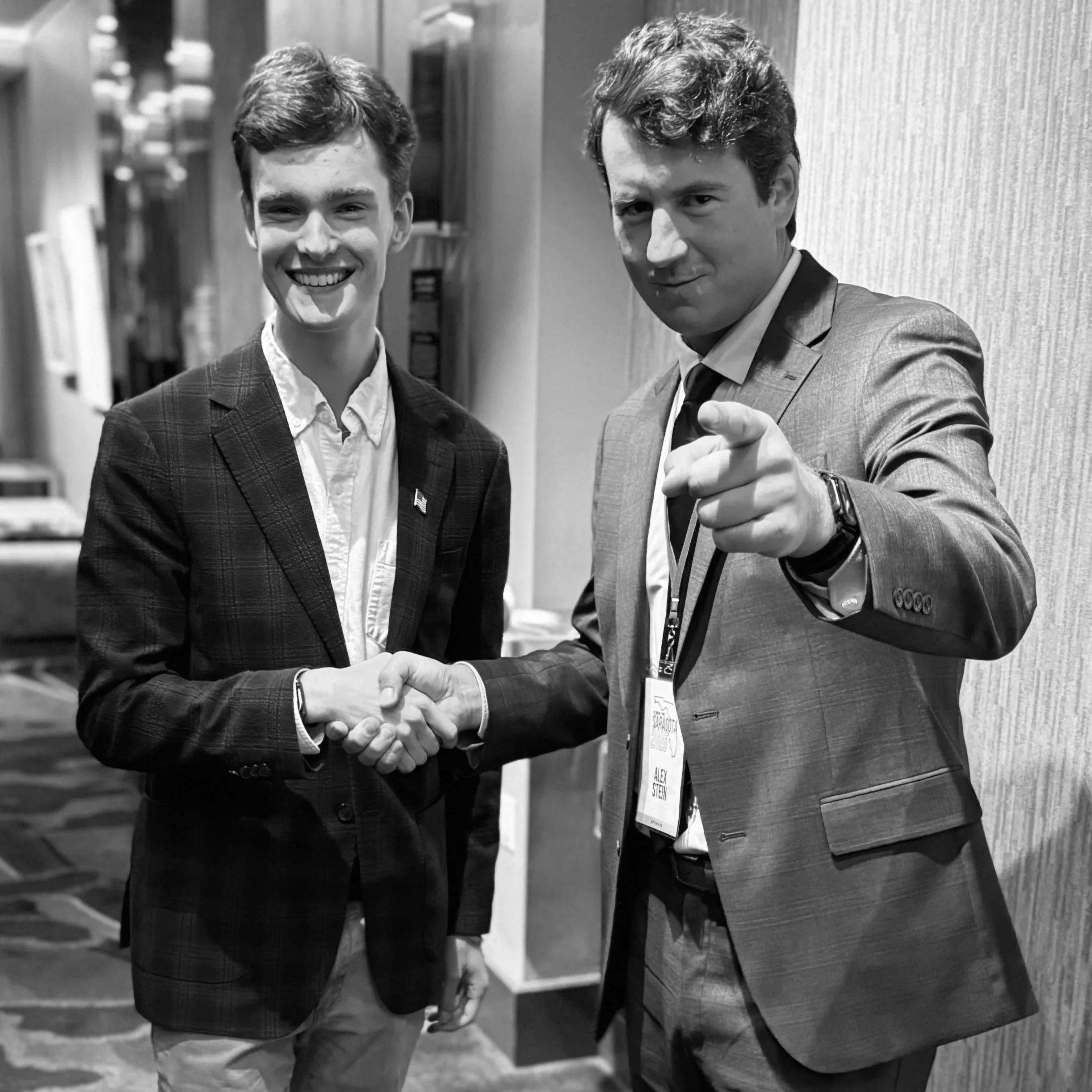 Alex Schneider and Alex Stein are shaking hands and smiling.