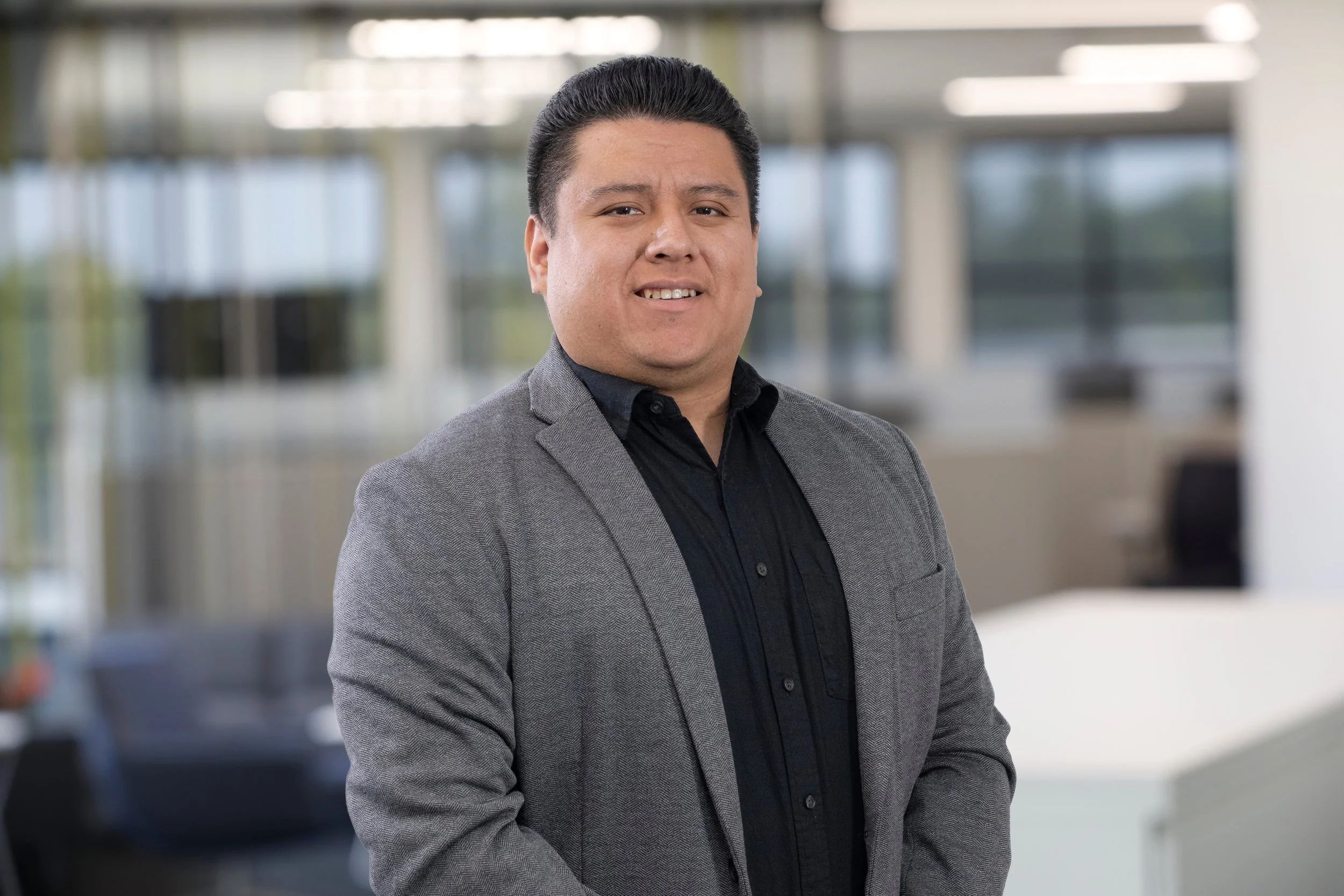 Isaac Ruiz is standing in modern office with large windows and a blurred background.