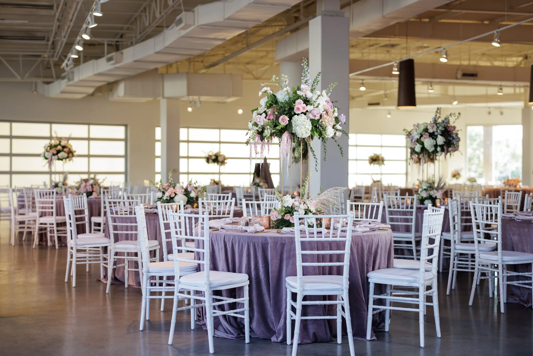 Elegant wedding reception setup with tall floral centerpieces and white chairs at Level Two Events, a modern Dallas wedding venue.