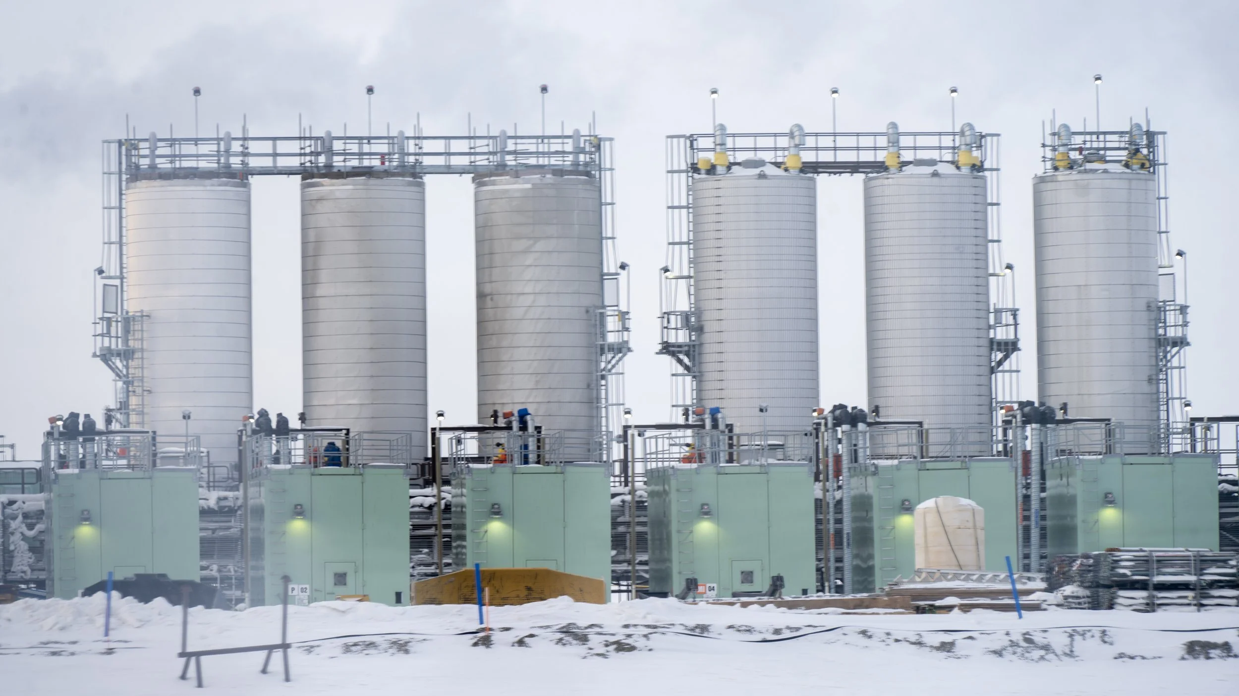 Industrial facility with large white storage tanks in a snowy environment.
