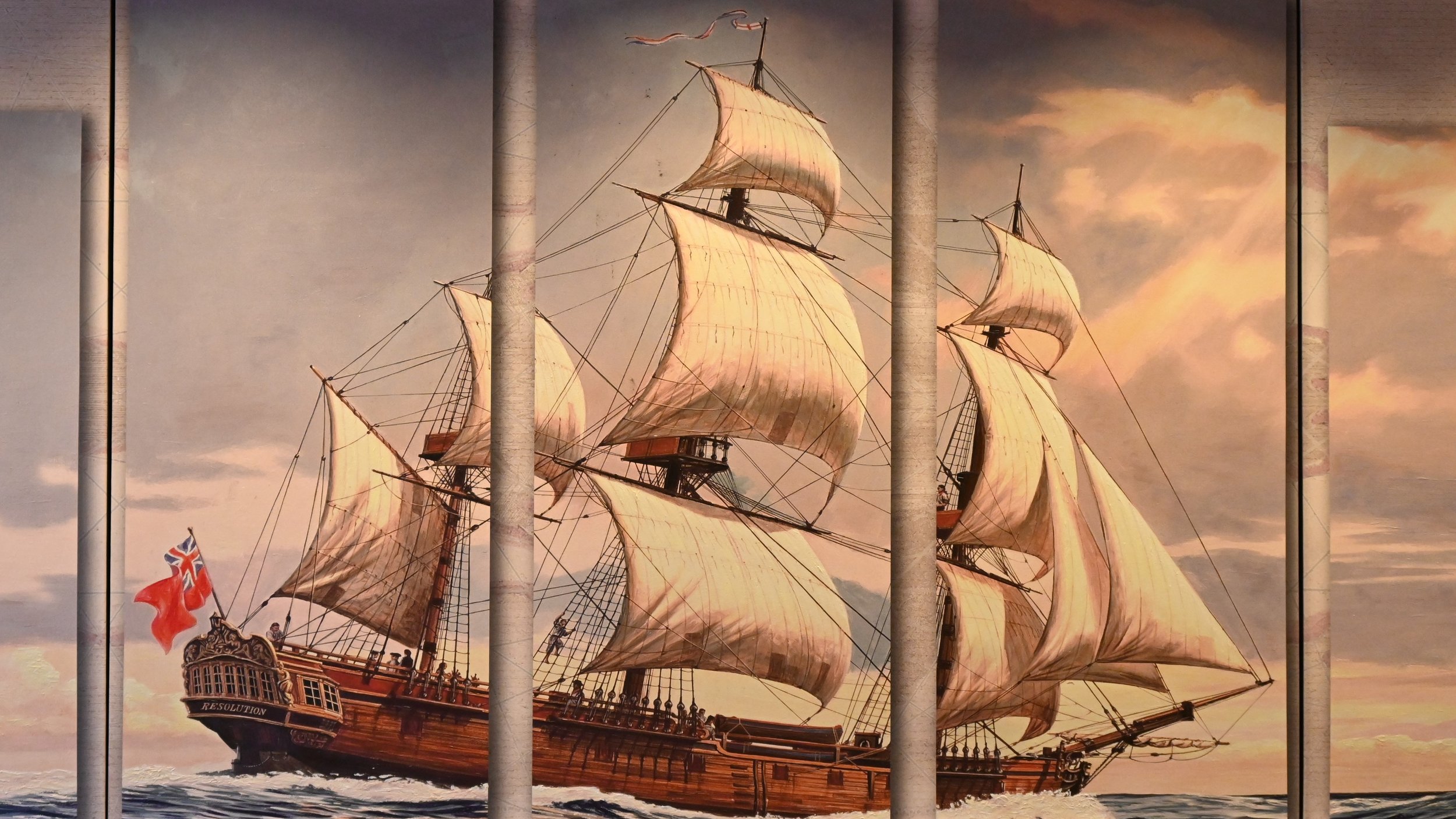 Painting of a large sailing ship with multiple sails, flying a British flag, viewed through a window with vertical bars, at sunset or sunrise with a cloudy sky.