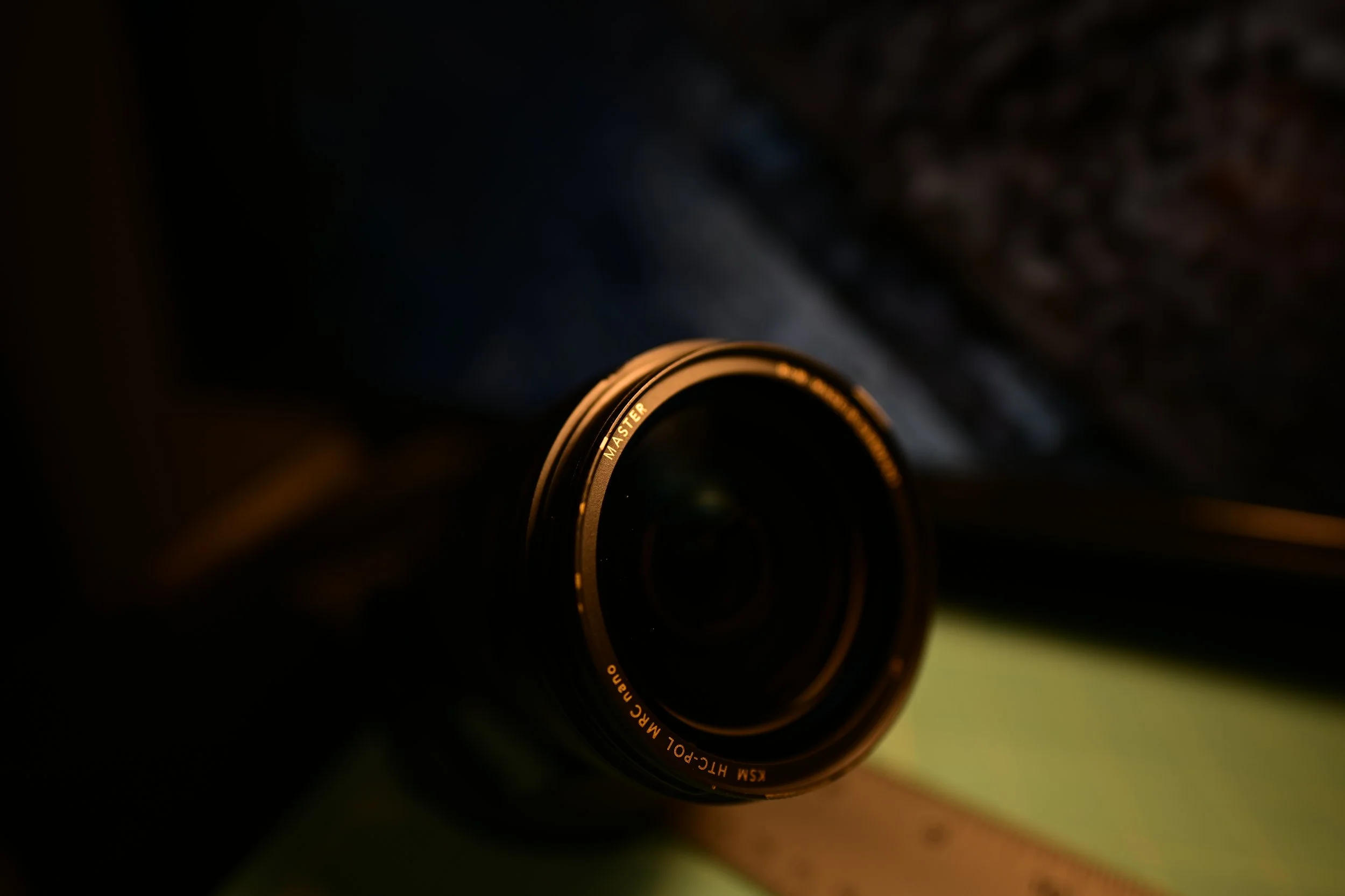 Close-up of a camera lens in a dark setting, with some light reflecting off the lens rim.
