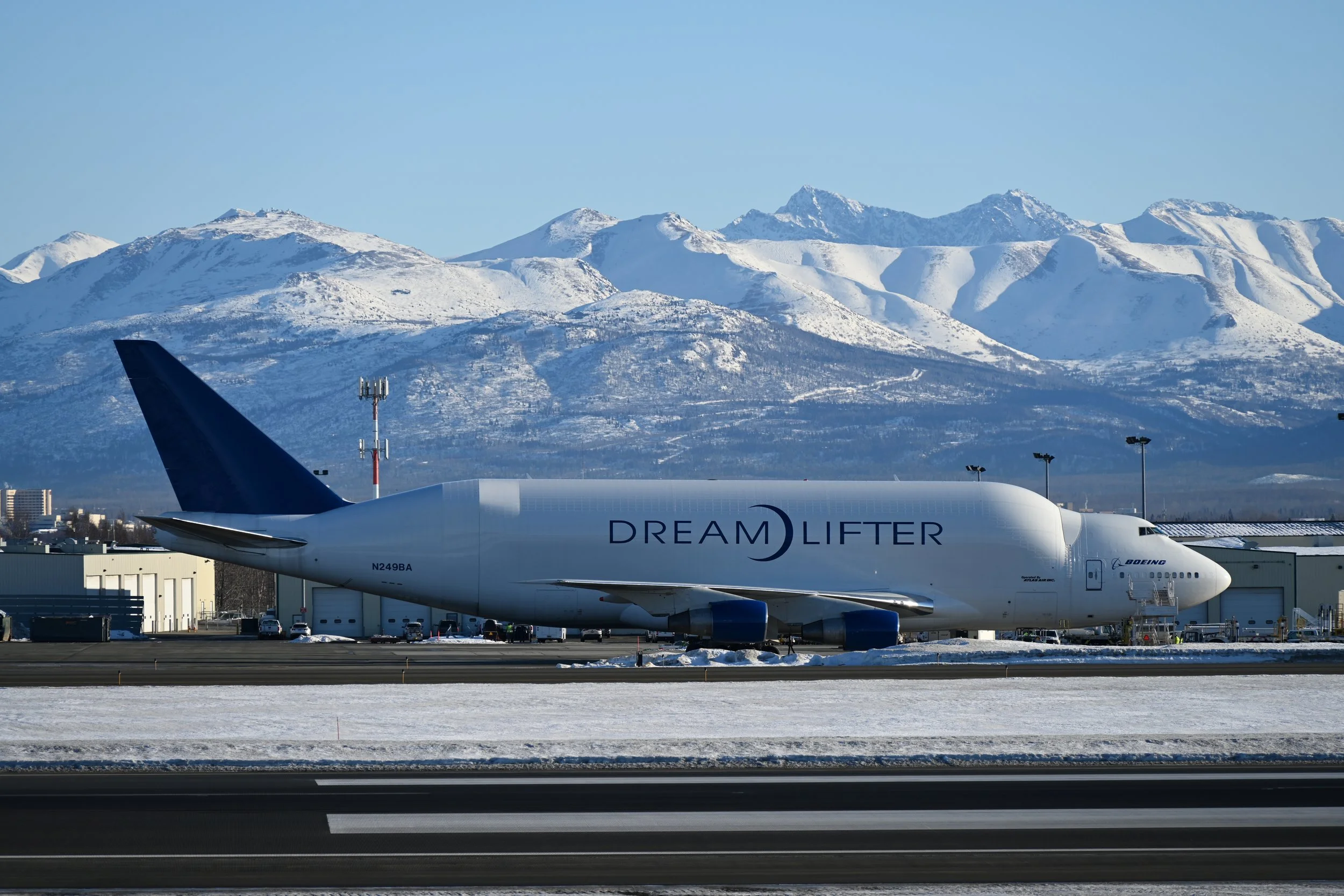 Commercial airplane on runway with snow-covered mountains in the background, labeled 'DREAM LIFTER' and 'BOEING'.