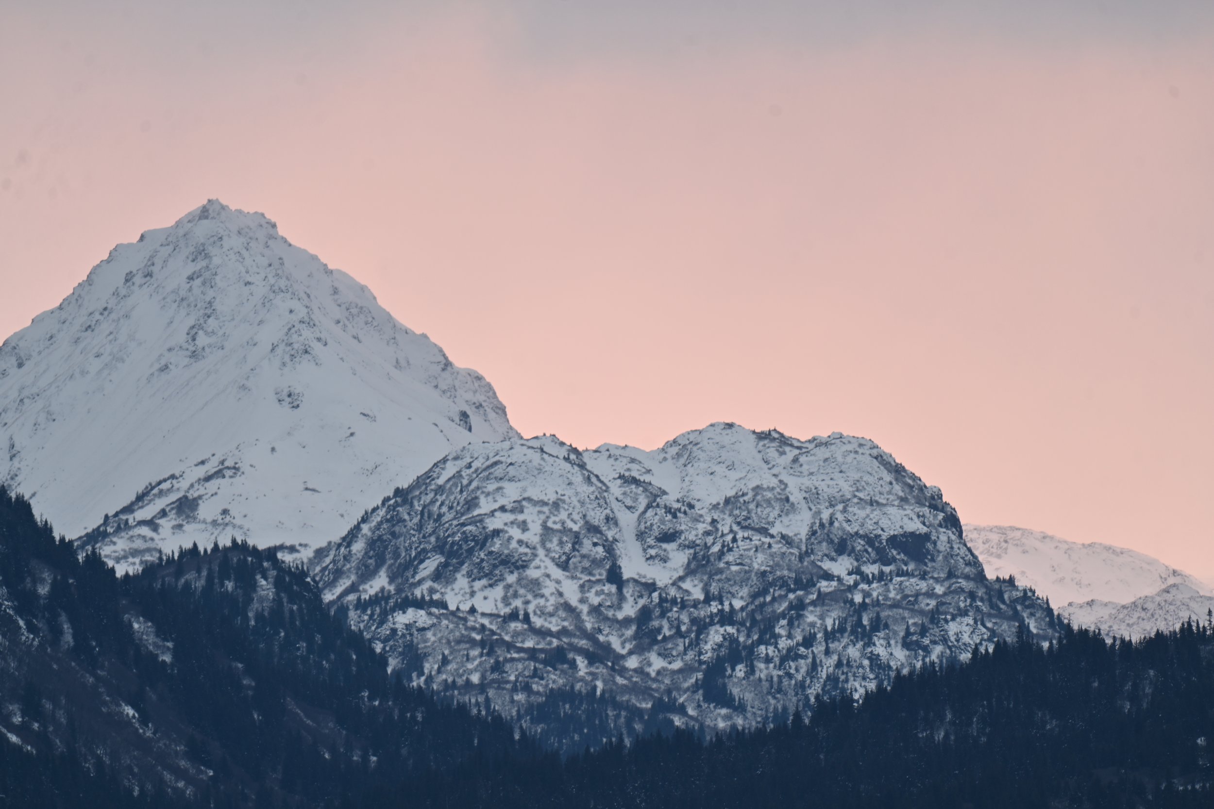 Snow-covered mountain range at sunset with a pink sky.