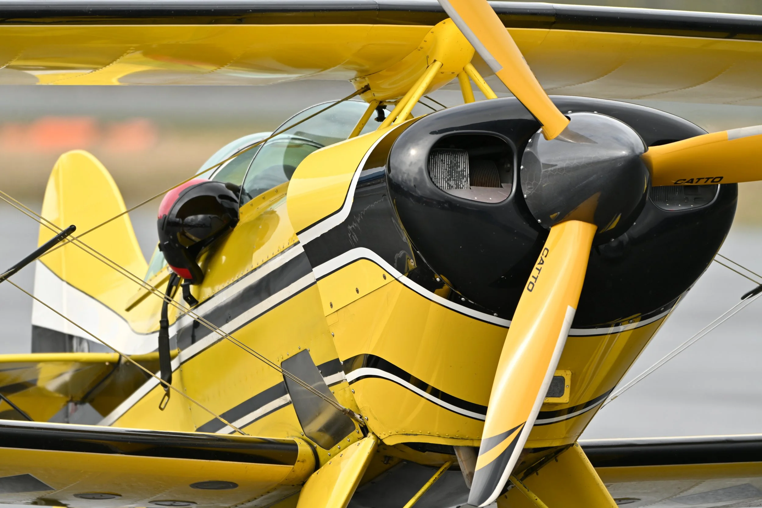 Close-up of a yellow and black aerobatic aircraft with a propeller and pilot helmet, ready for flight.