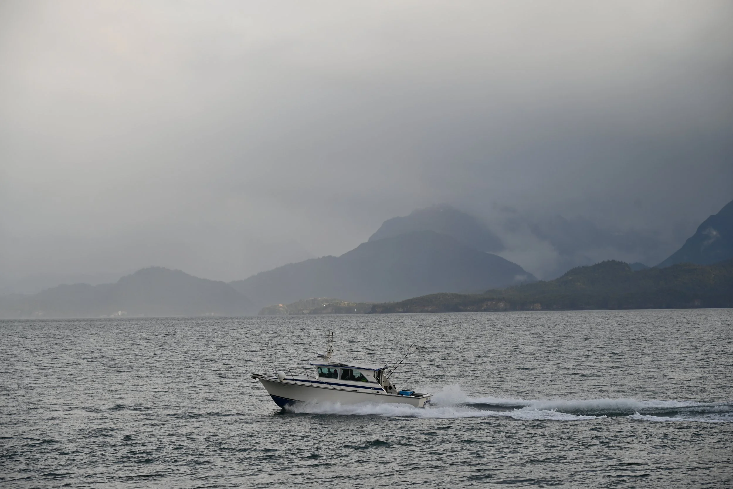 A boat cruising on a body of water with mountains and cloudy sky in the background.