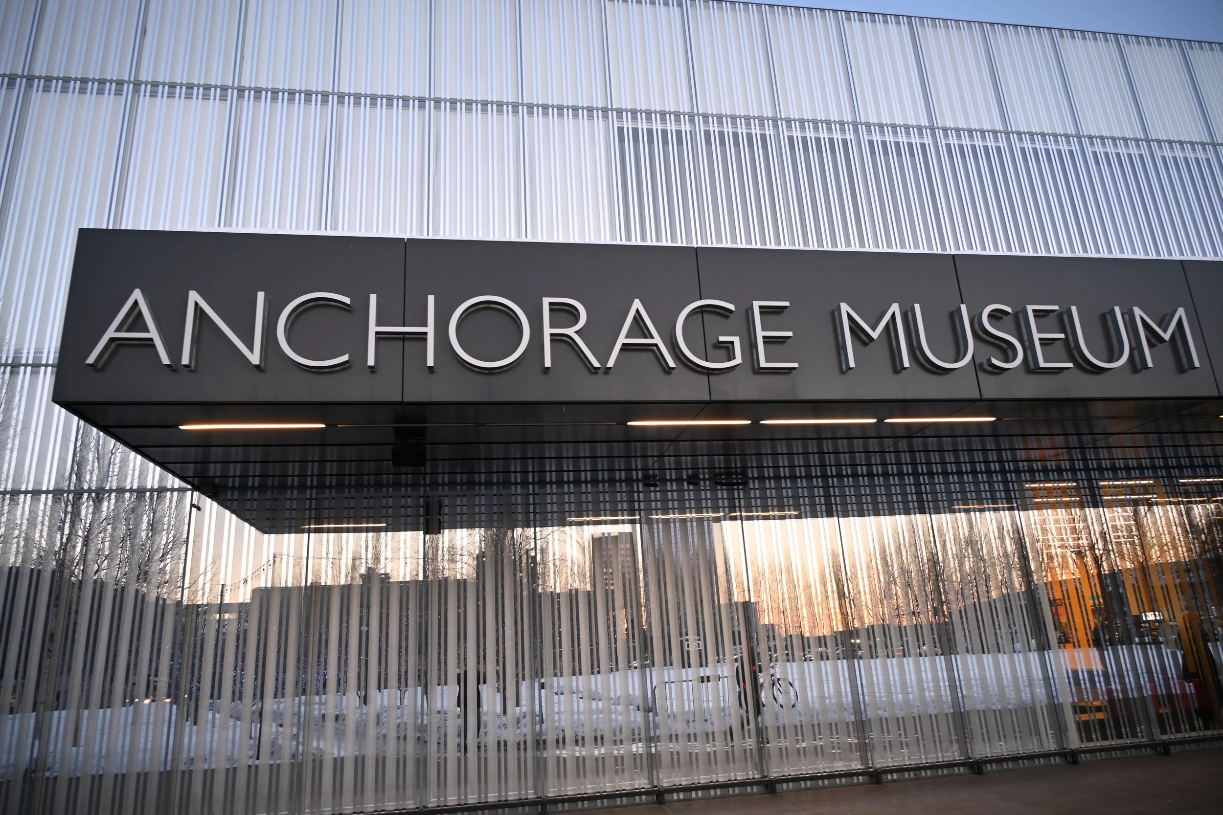 Exterior view of the Anchorage Museum showing its modern facade with vertical metal strips and the museum's name displayed prominently.
