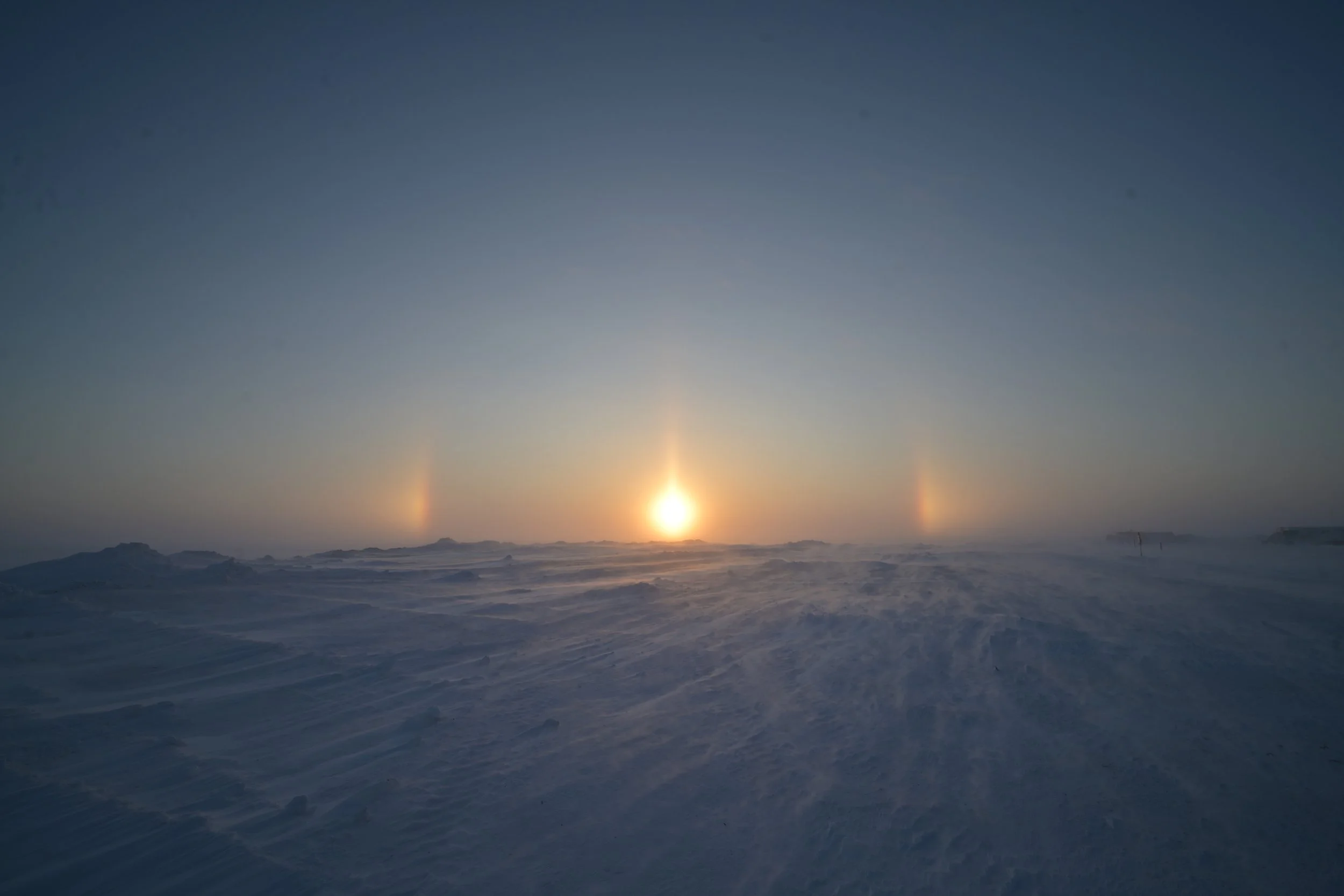 Sun setting over a snowy landscape with sundogs visible in the sky.