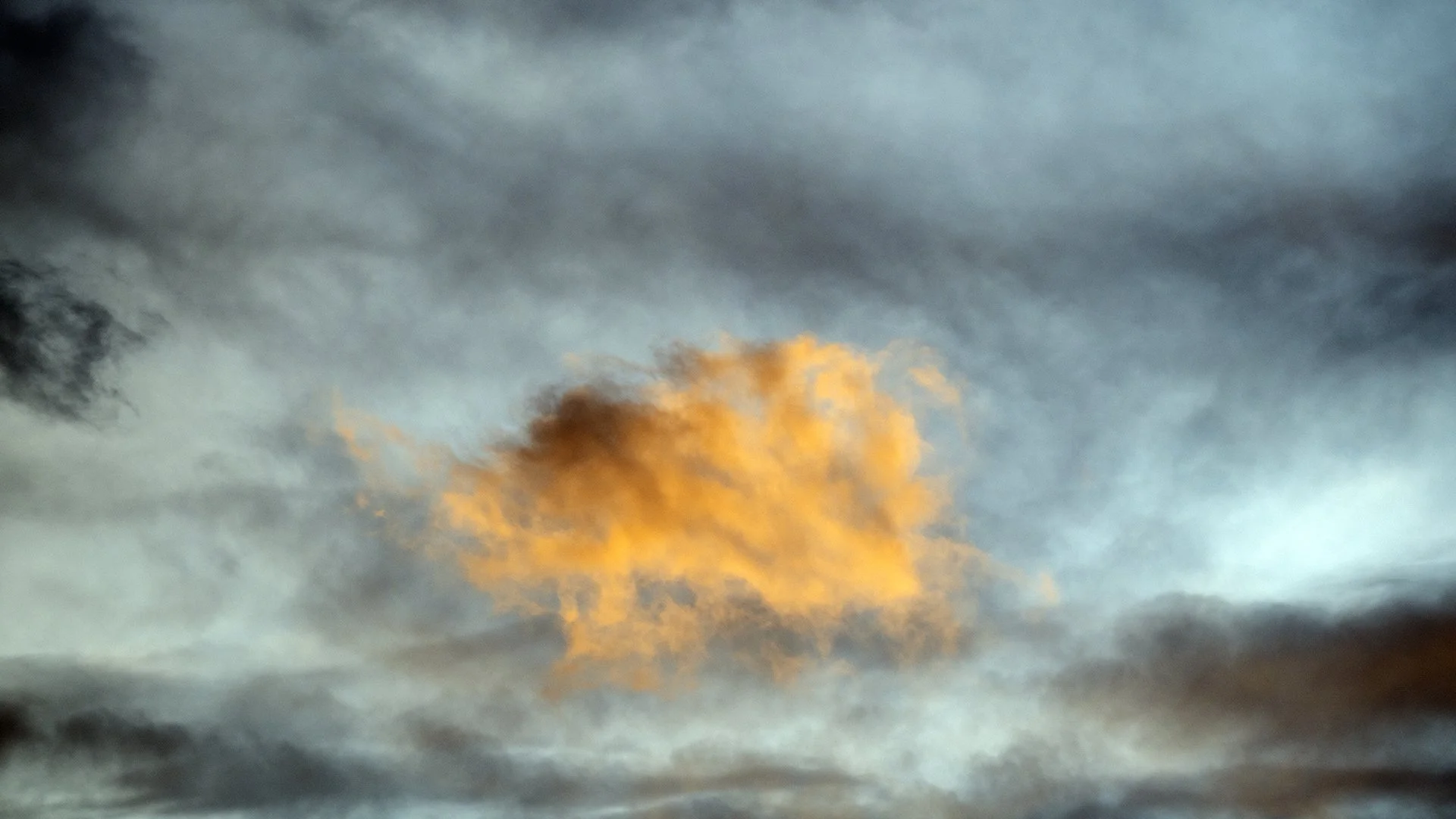 A sky filled with dark gray clouds and a single, bright orange cloud illuminated by sunlight.