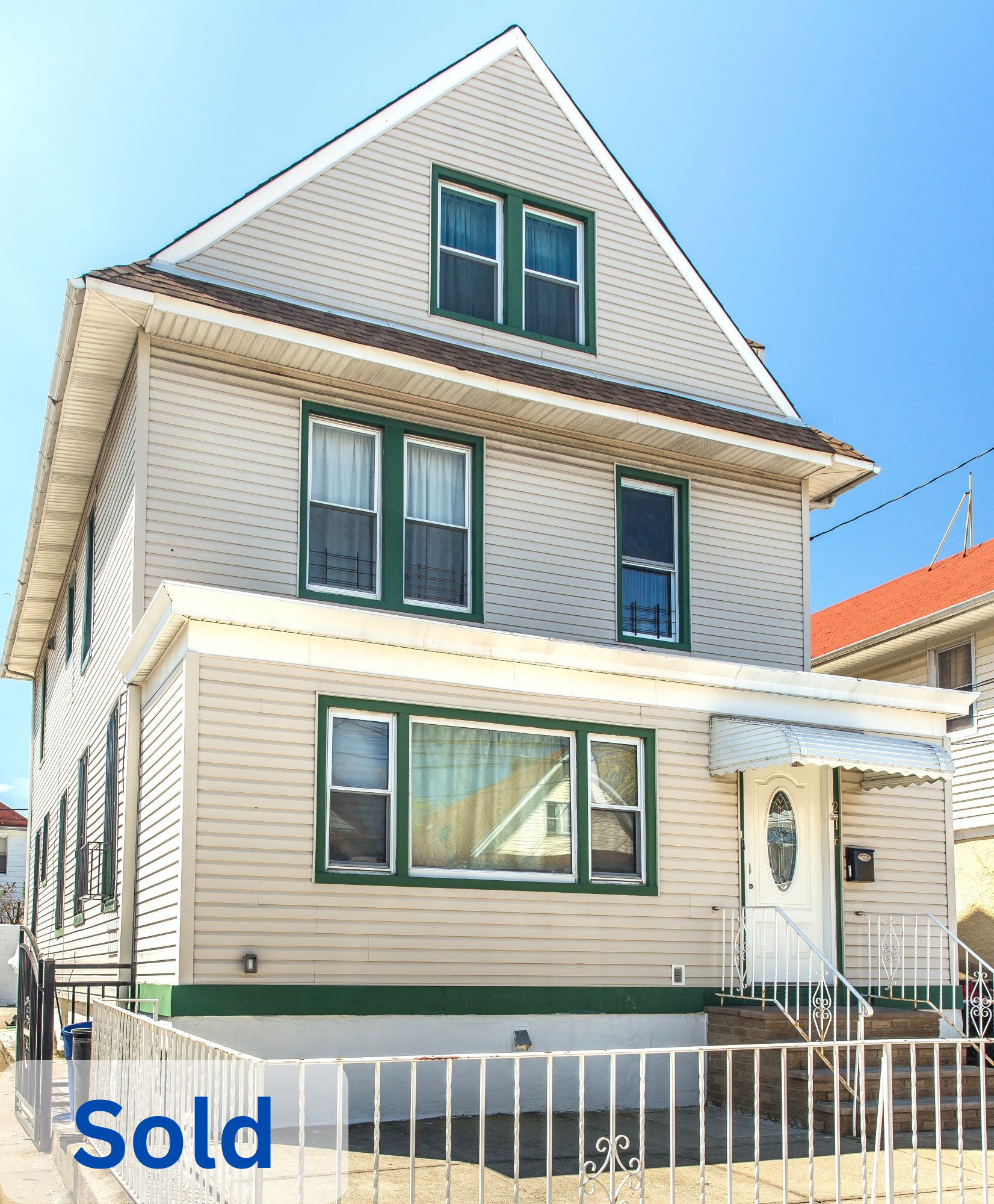 Three-story house with beige siding, green window frames, and a small front porch with white railing. The house is marked as sold in blue text.