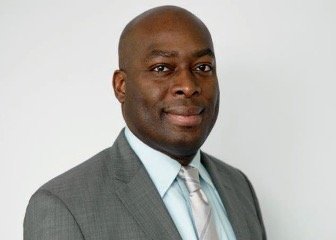 Professional man in gray suit and light blue shirt, looking at camera against a plain white background.