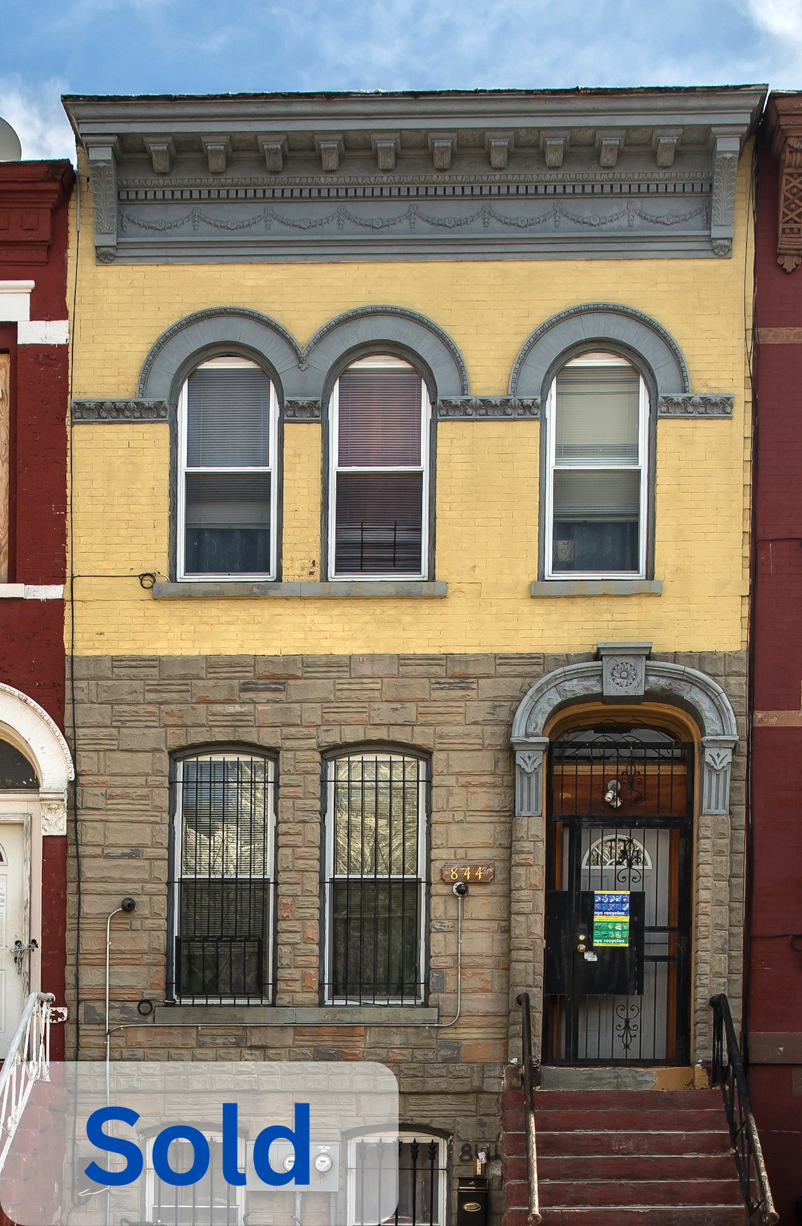 Three-story row house with yellow upper facade and brick lower facade, featuring arched windows with gray trim, black iron bars, a black front door with decorative arch and ironwork, stairs with black railings, and a "Sold" overlay.