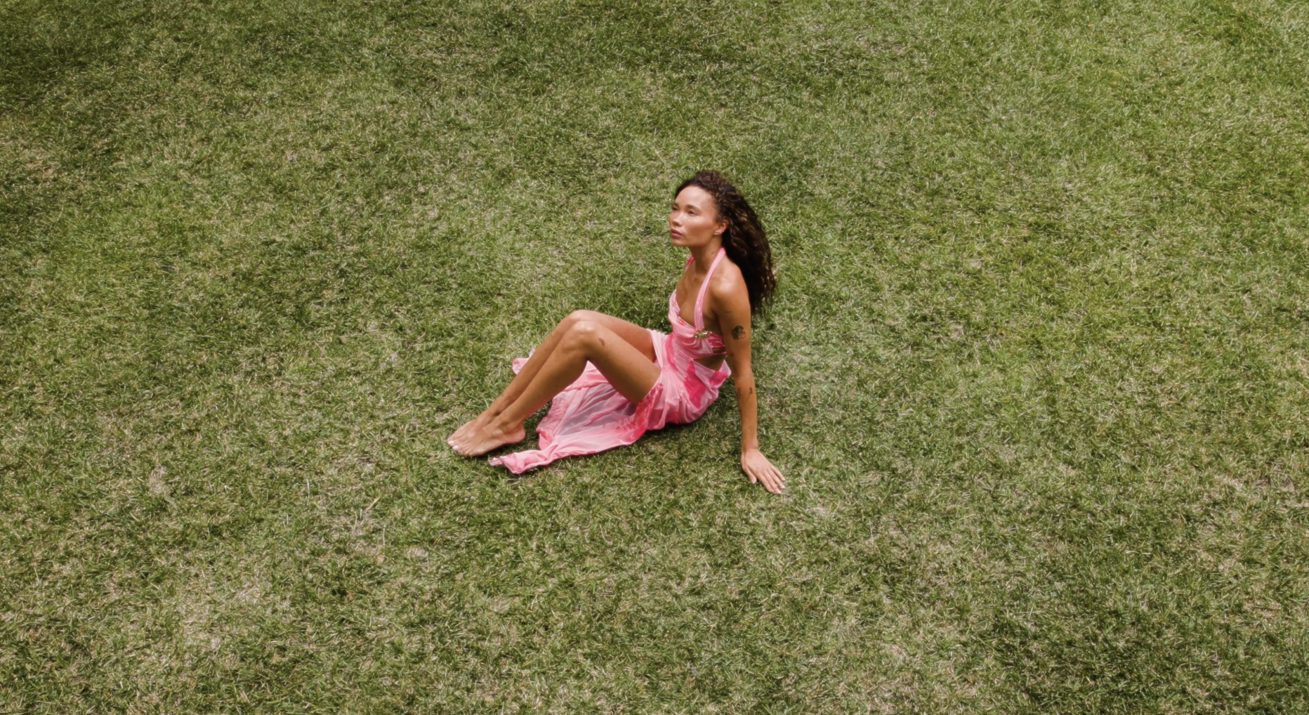 Woman in pink dress sitting on grass field