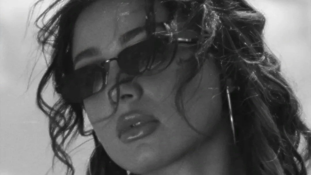 Close-up black and white photo of a woman with curly hair wearing dark sunglasses and hoop earrings.