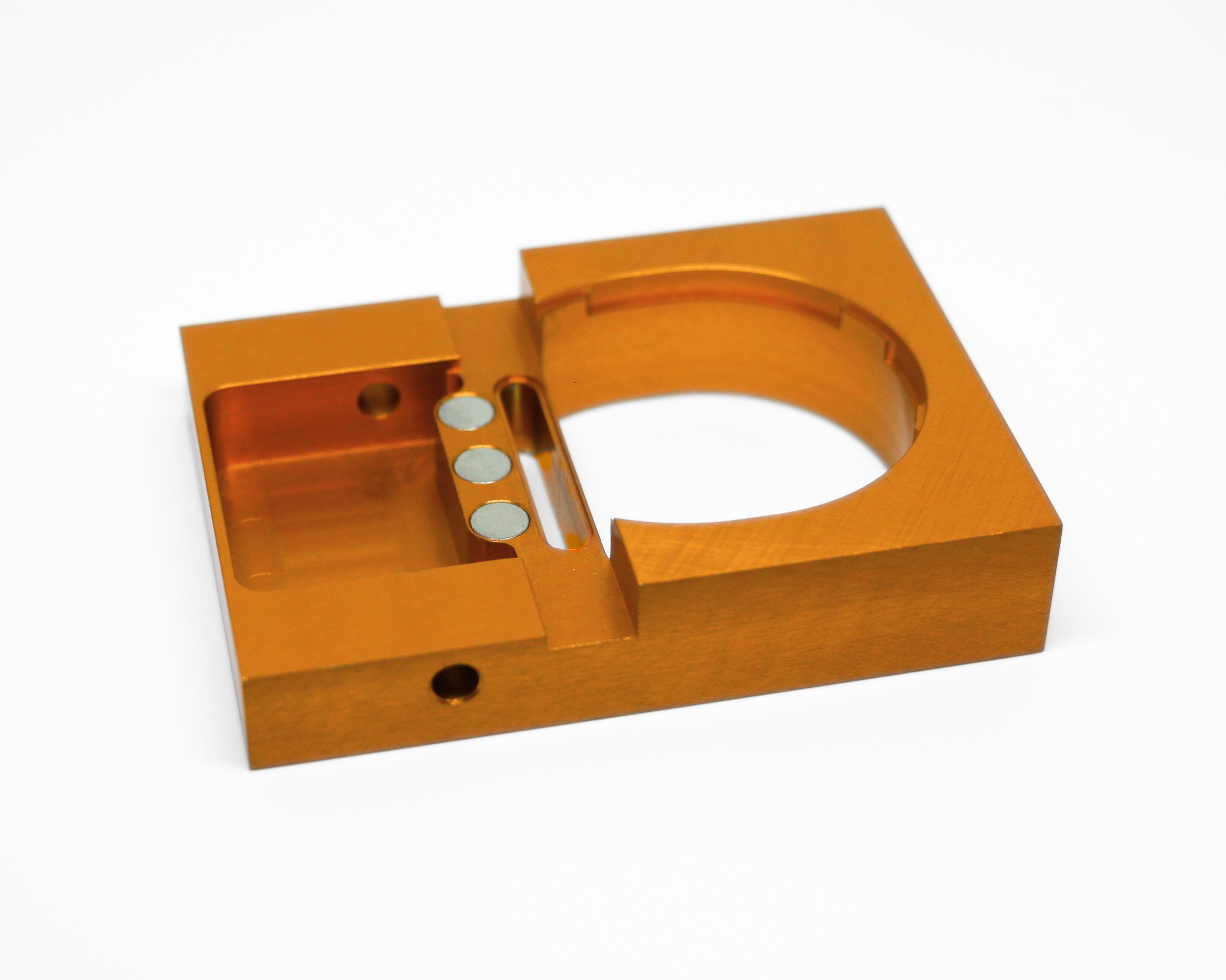 An orange metallic rectangular mechanical part with a circular cutout and small inner holes, placed on a white background.