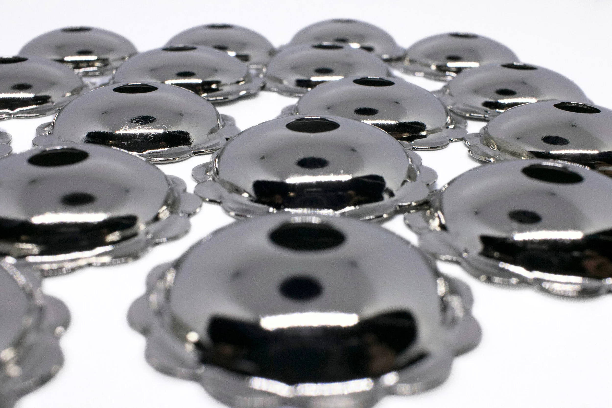 Multiple shiny metal buttons with black holes in the center, laid out on a white surface.