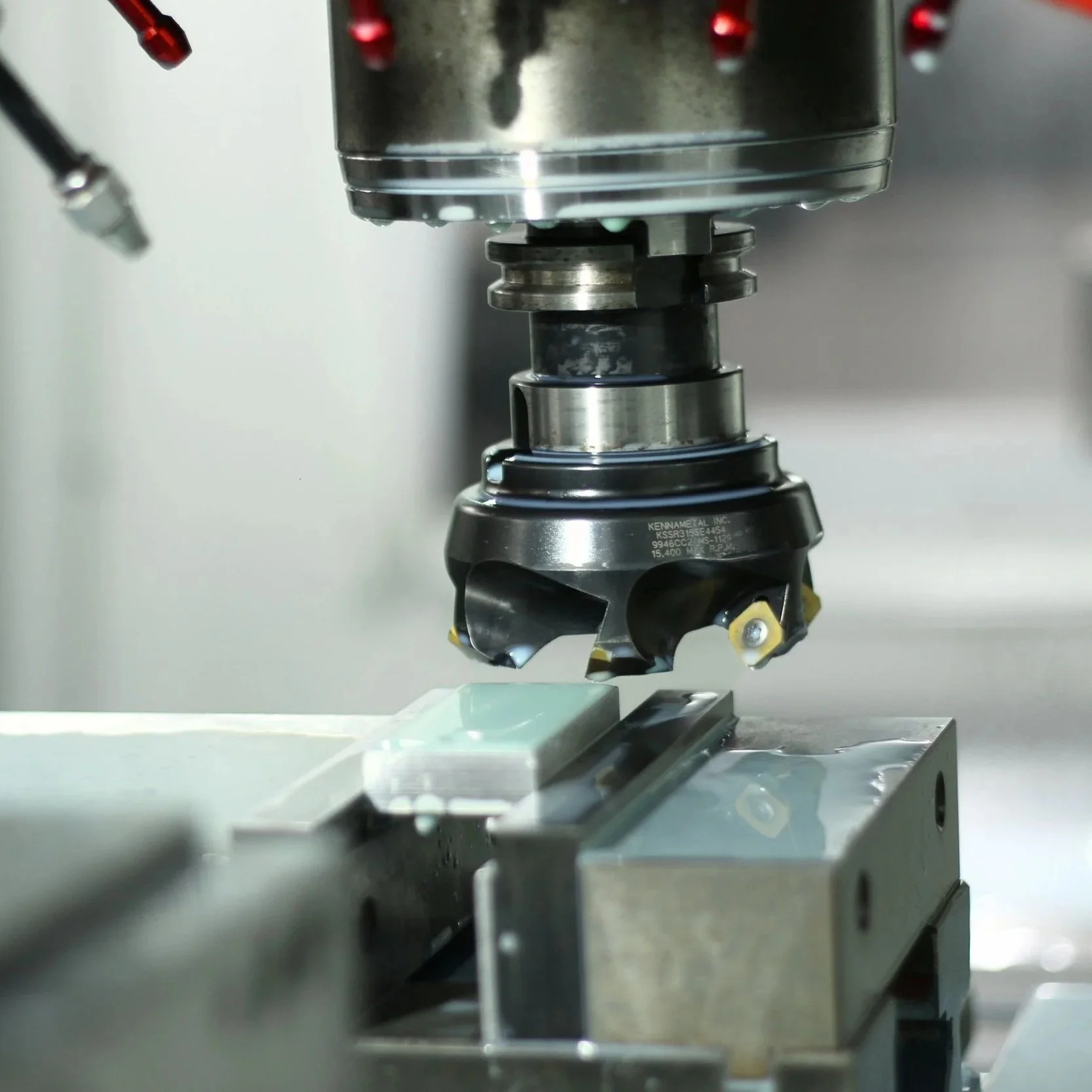 A close-up of a CNC machine cutting or engraving a material with a spinning tooling at the bottom, positioned over a metal workpiece.