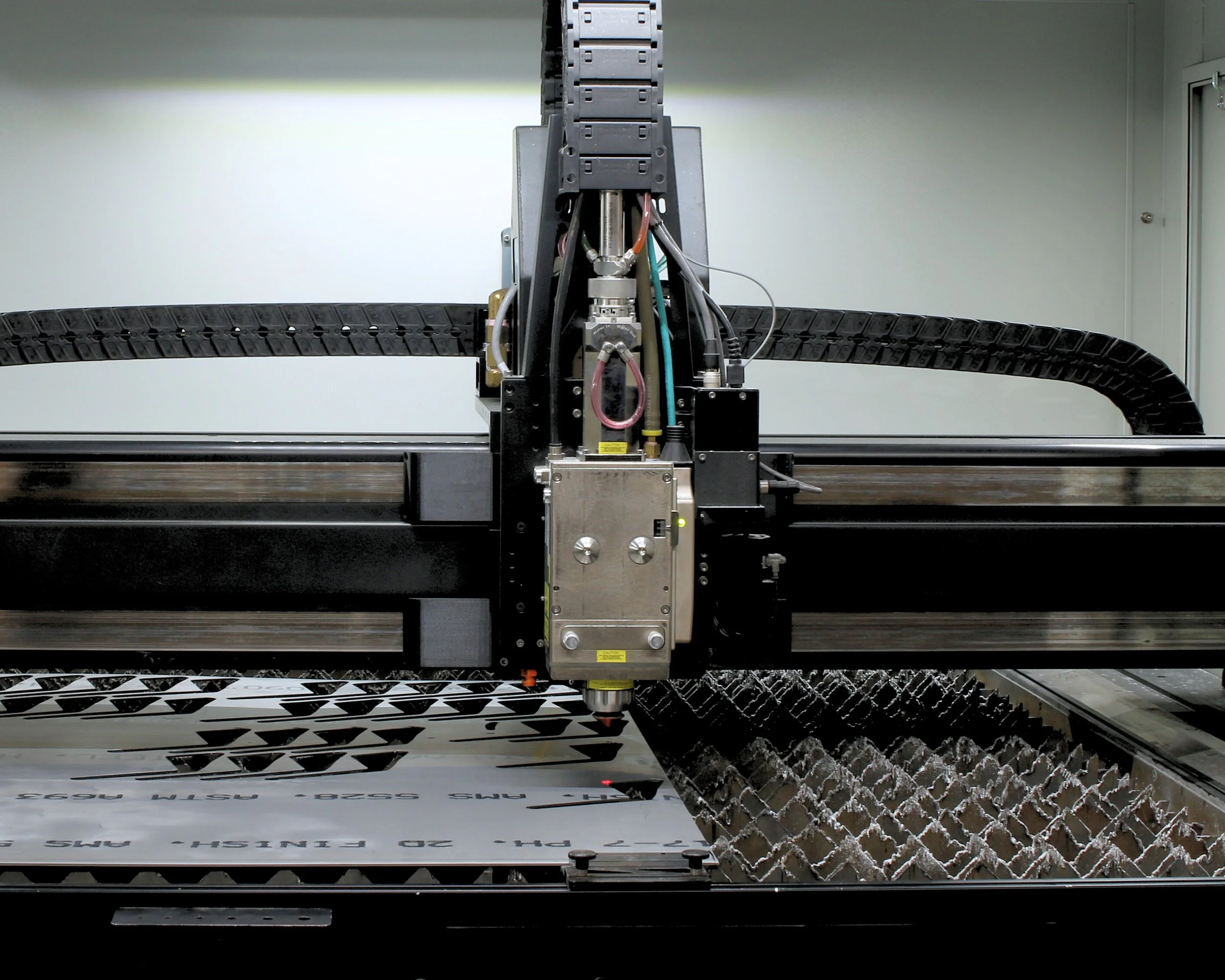 Close-up of a CNC laser cutting machine cutting a sheet of metal with text and patterns, inside industrial setting.