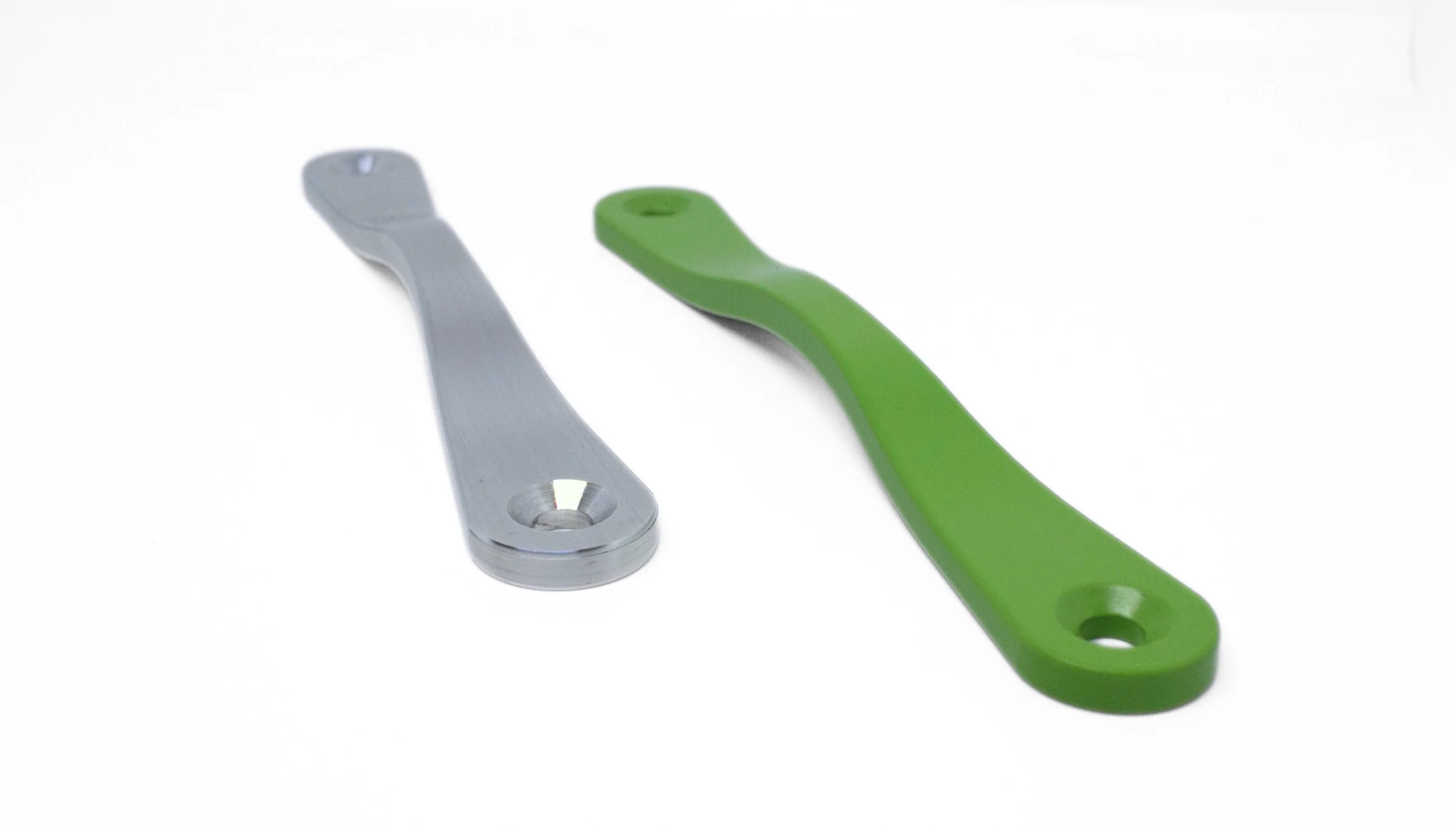 Two turn-safe opening tools, one metallic silver and one green, with curved handles and circular openings at the ends, on a white background.