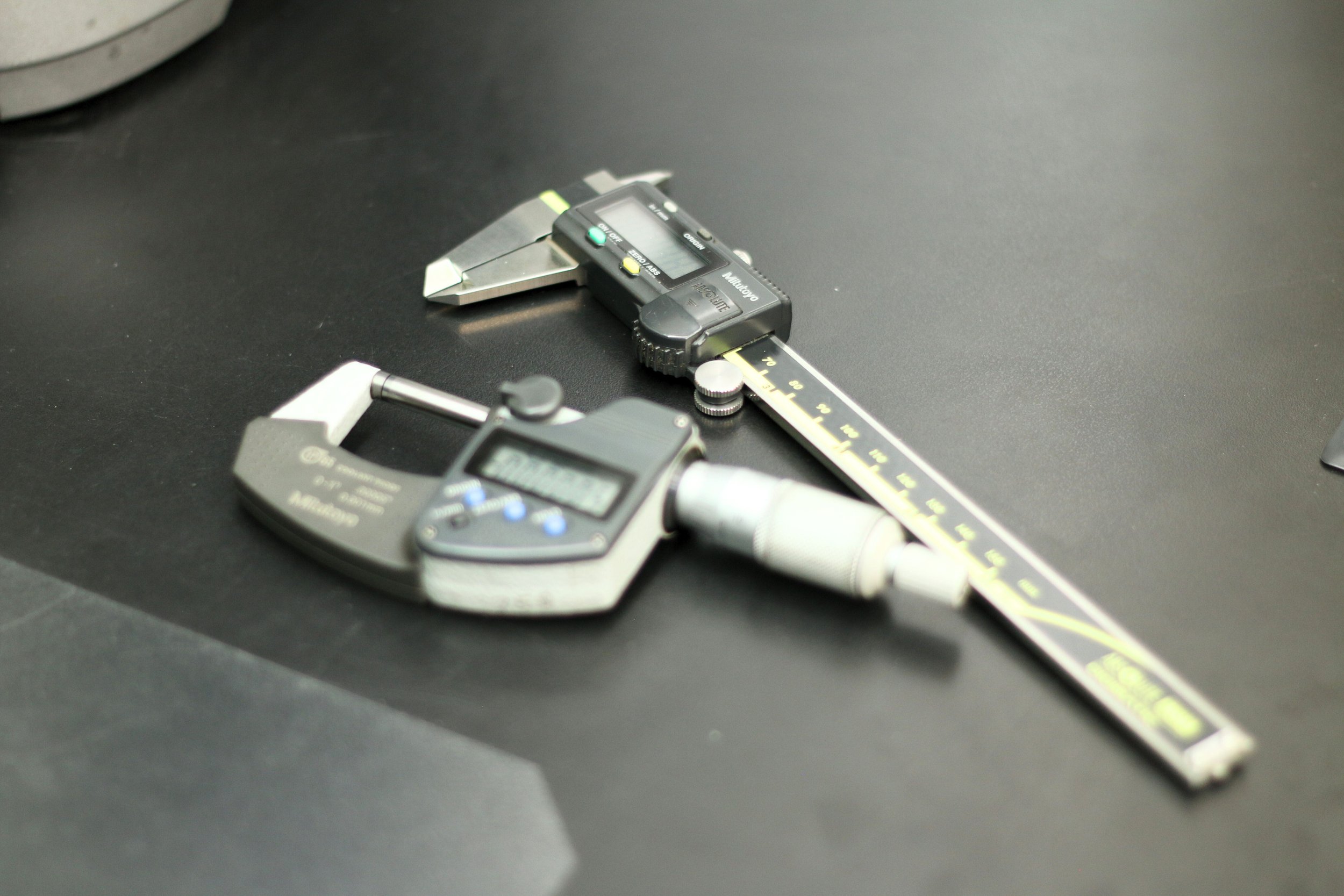 Digital calipers and a dial gauge measuring instrument on a black work surface.
