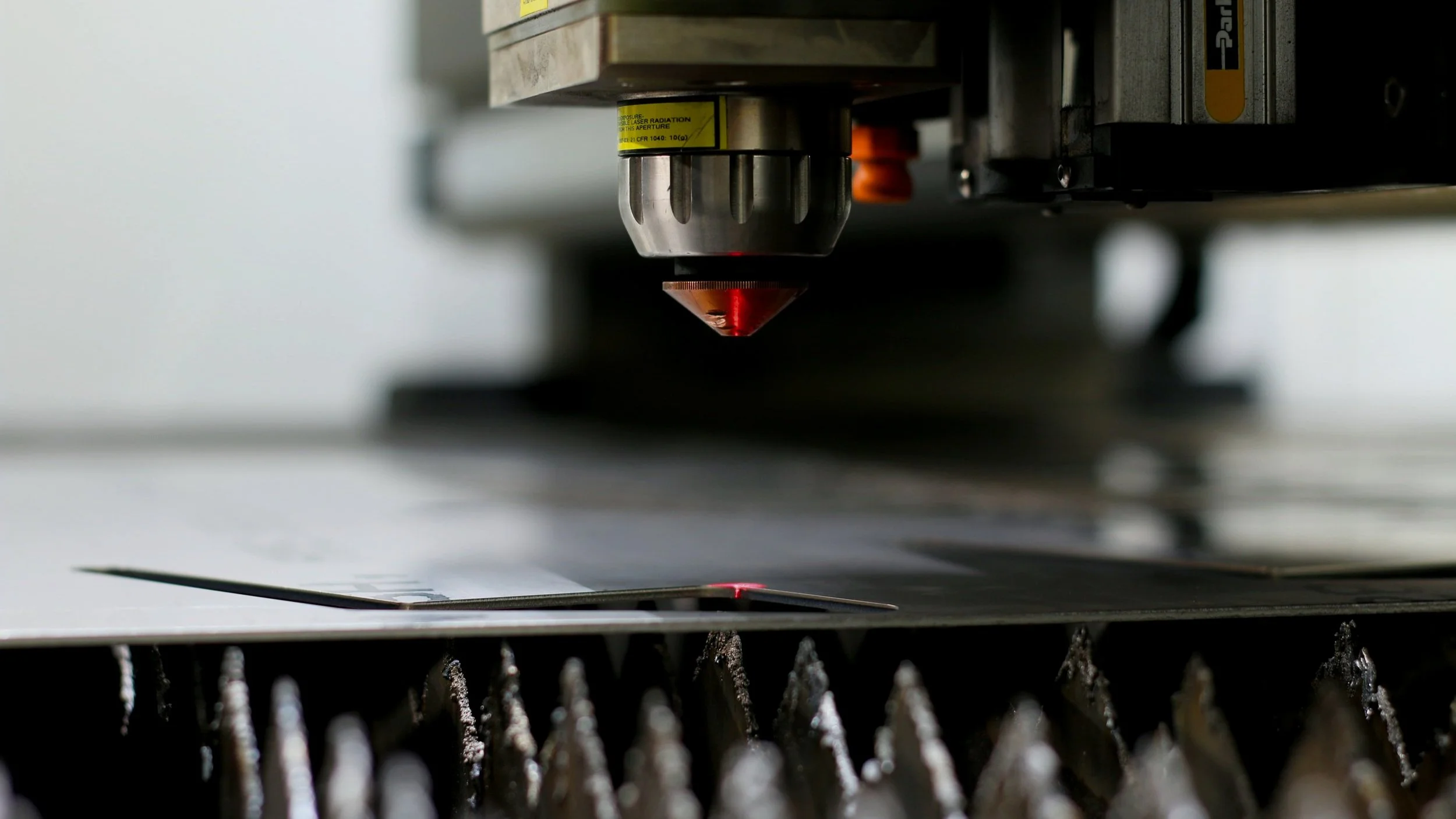 Close-up of a laser cutting machine's nozzle emitting a red laser beam onto a metal sheet.