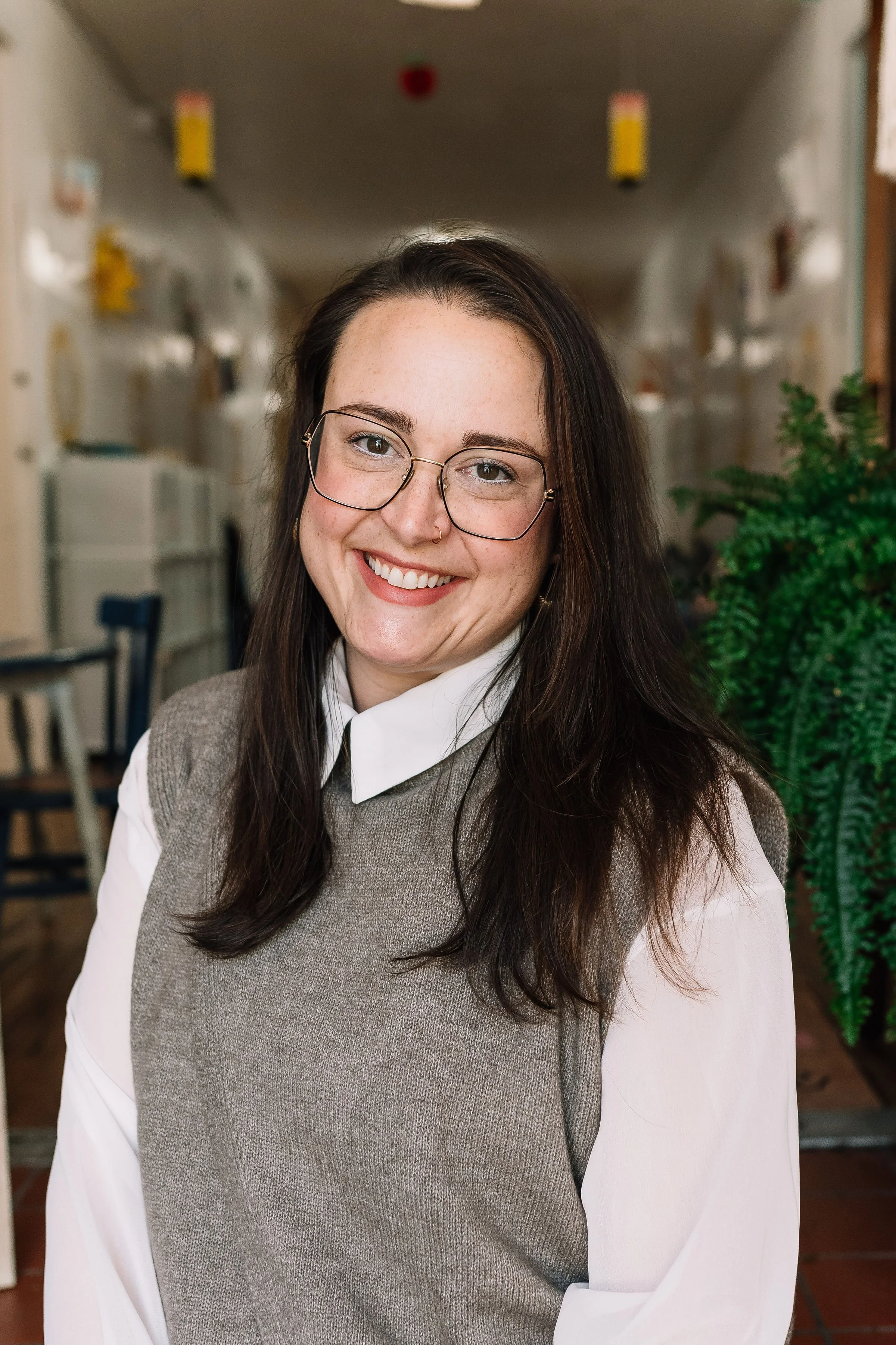 Smiling woman with curly hair, glasses, earrings, and layered necklaces, wearing a striped blouse.