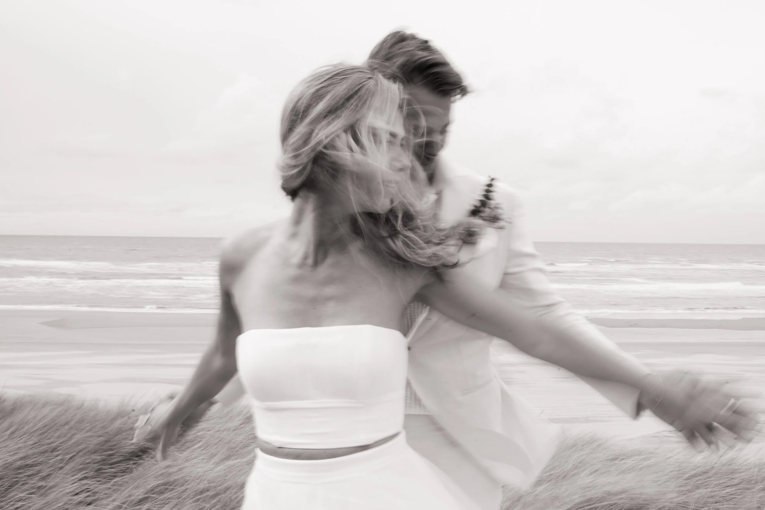 A bride and groom holding hands on a beach, with the bride's veil flowing in the wind.