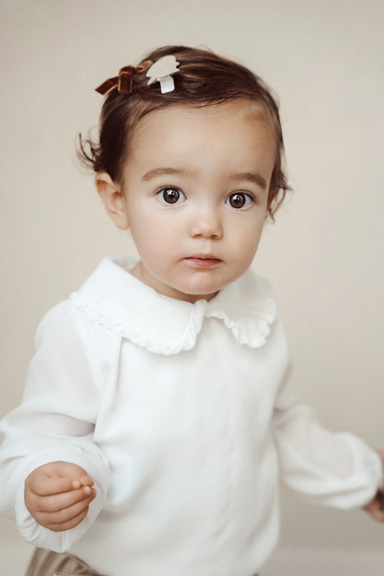 A young girl with brown hair, large eyes, and a white blouse with a ruffled collar, looking at the camera.