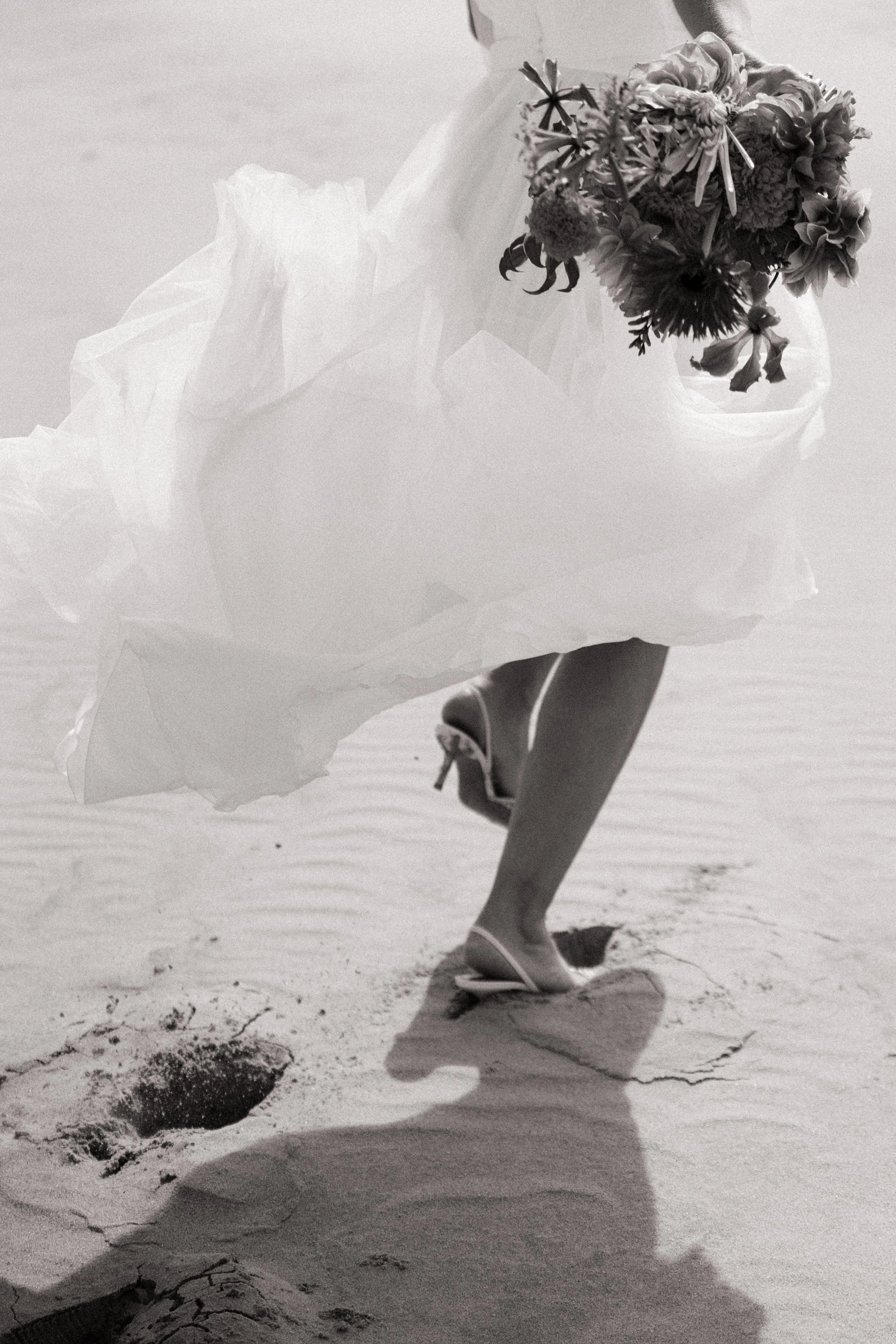 A bride and groom holding hands on a beach, with the bride's veil flowing in the wind.