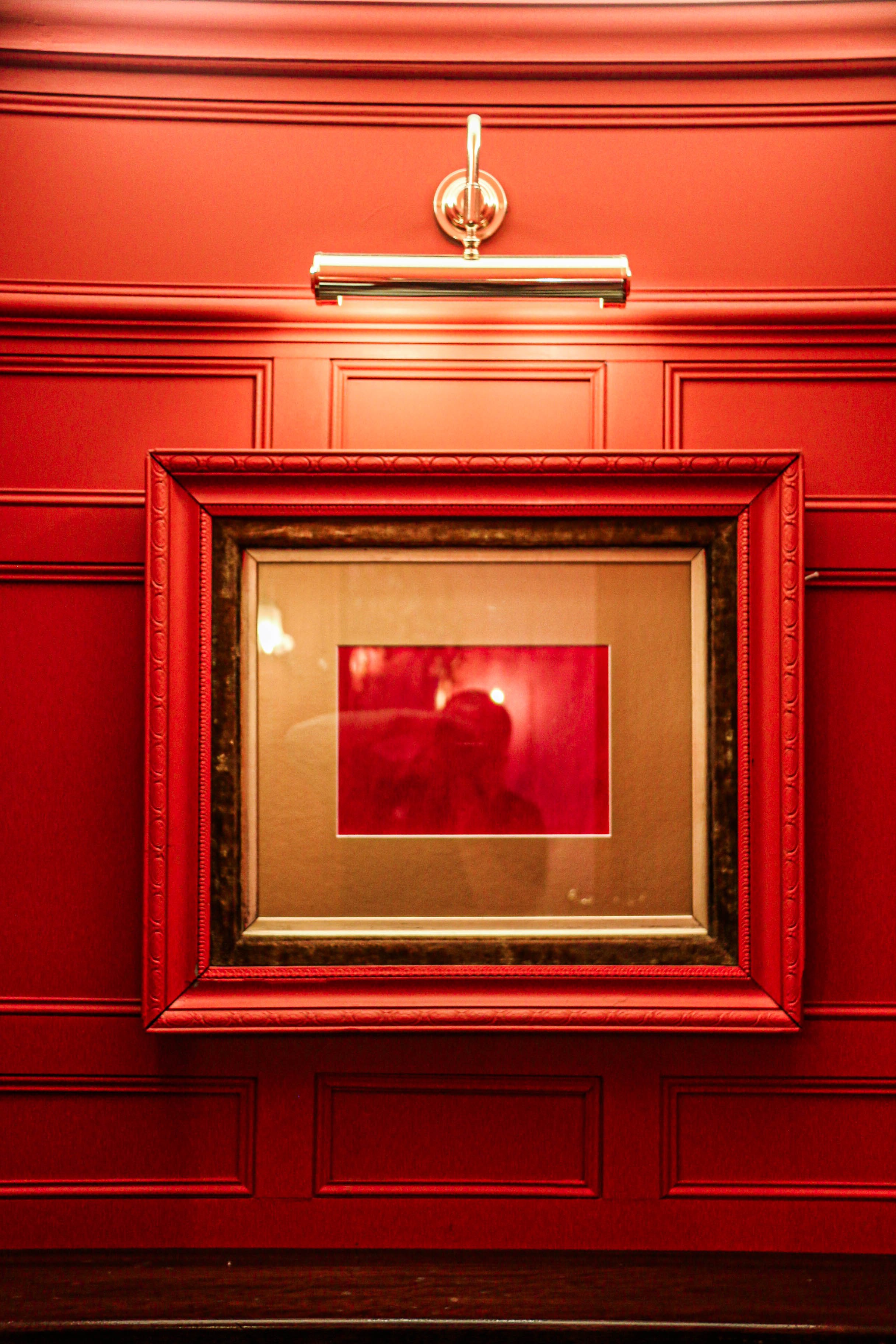Red-paneled wall with a framed mirror or photo, and a wall-mounted light fixture above.