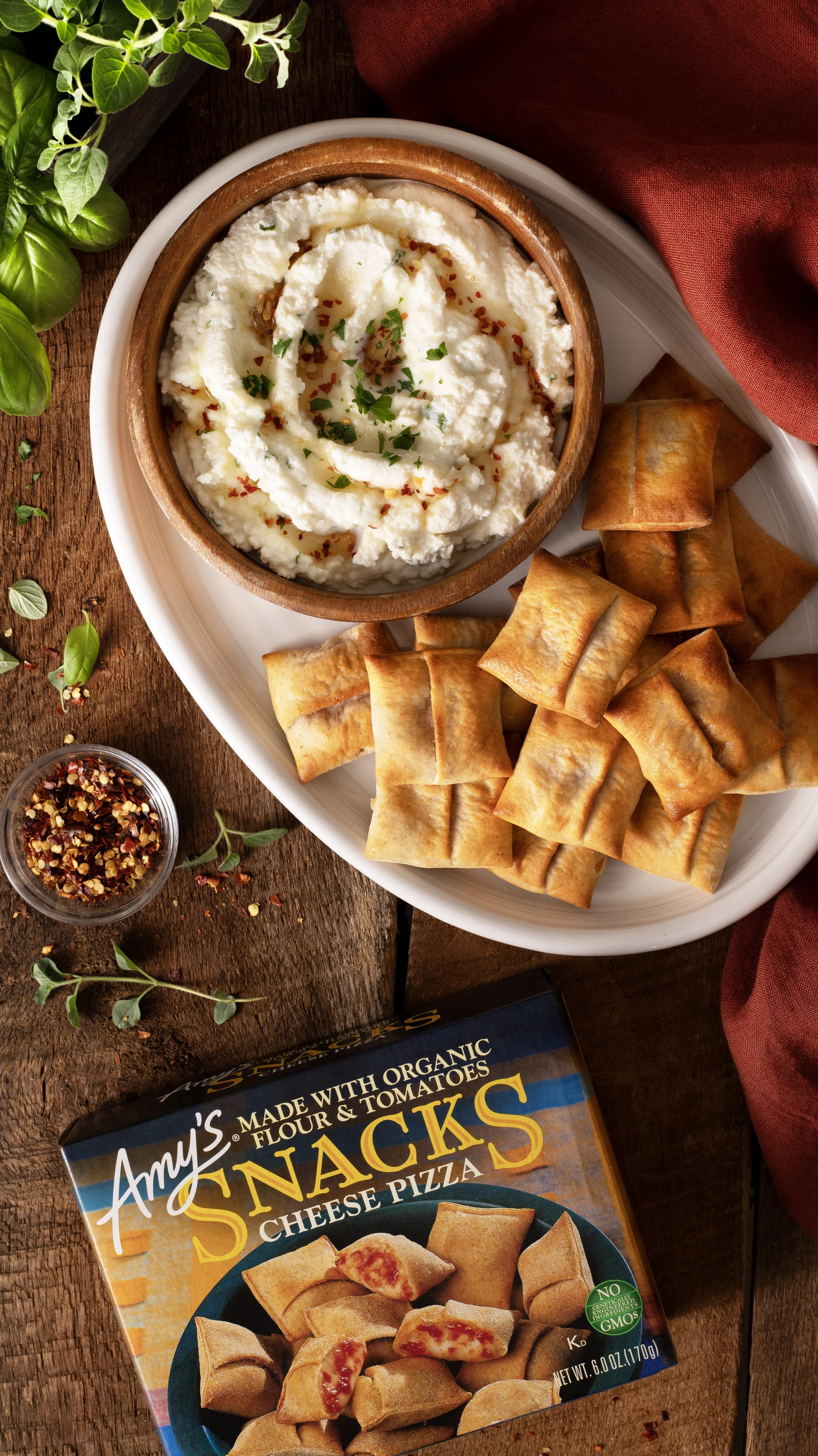 A plate of fried cheese sticks and a bowl of creamy mashed potatoes topped with herbs and red pepper flakes, with a box of Amy's cheese pizza snacks nearby.