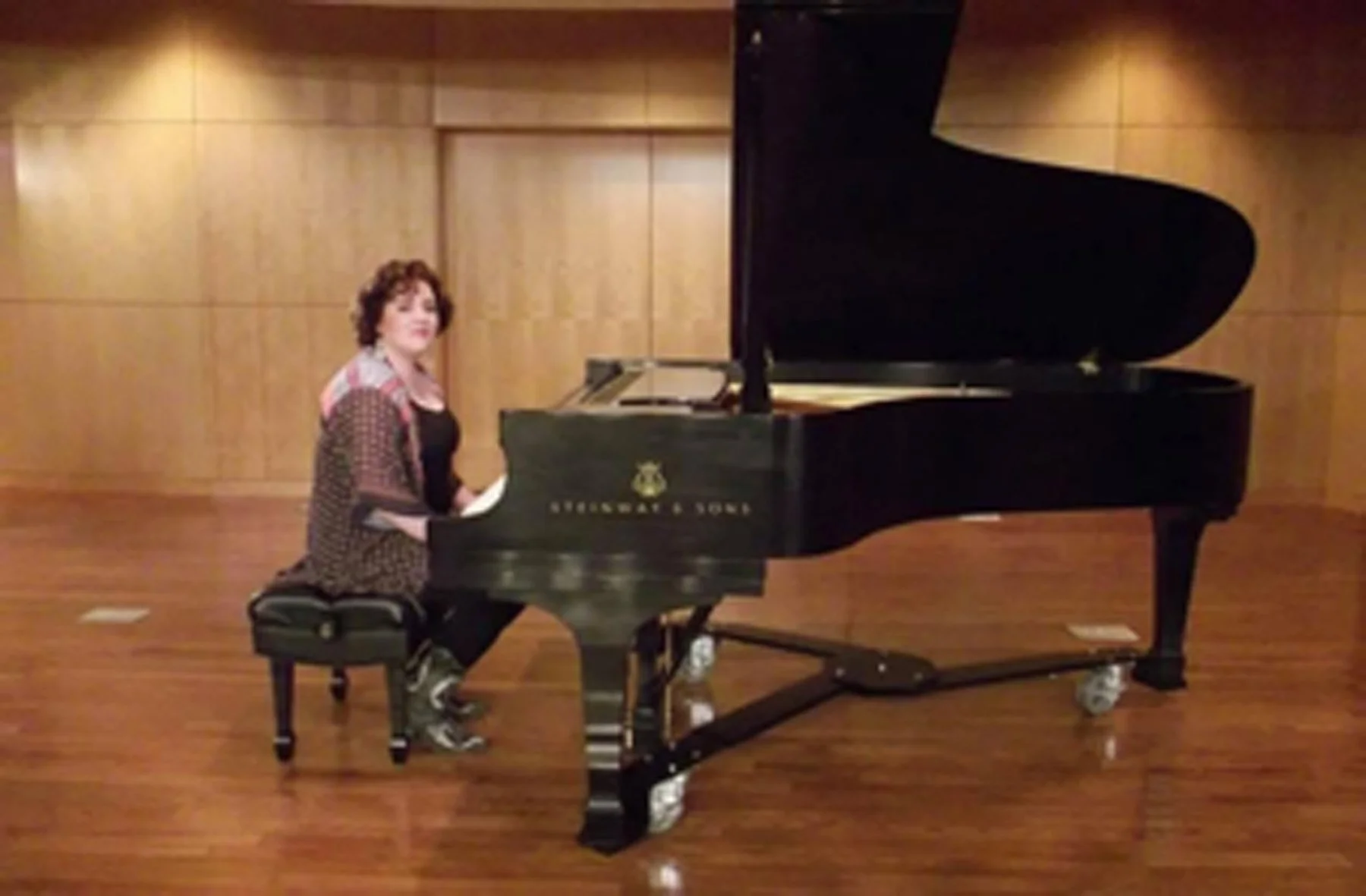 A woman sitting at a grand piano in a room with wooden walls and flooring.