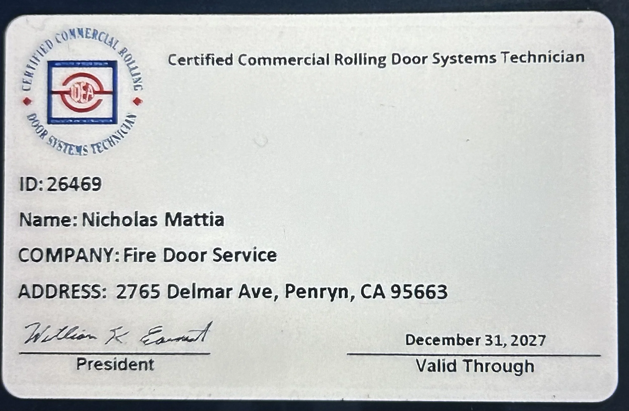 Identification card for a Certified Commercial Rolling Door Systems Technician named Nicholas Mattia from Fire Door Service, with ID 26469, located at 2765 Delmar Ave, Penryn, CA 95663, signed by William K. Esmond, dated December 31, 2027, and valid through an unspecified period.