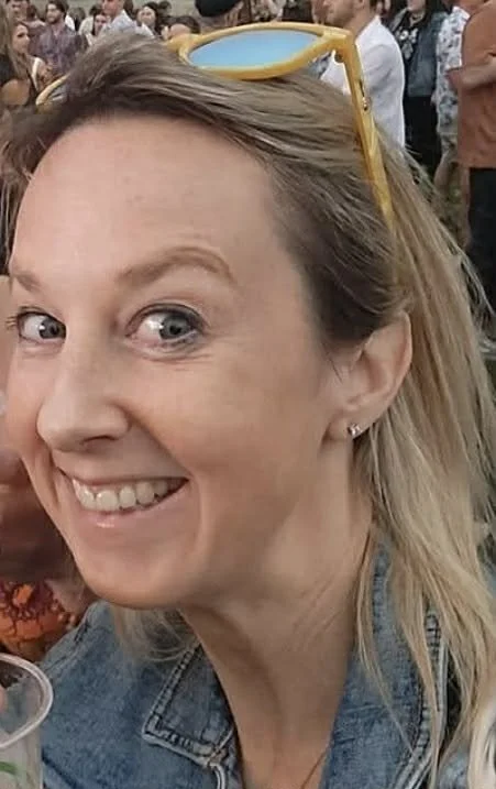A woman with blonde hair smiling at the camera against a plain background.
