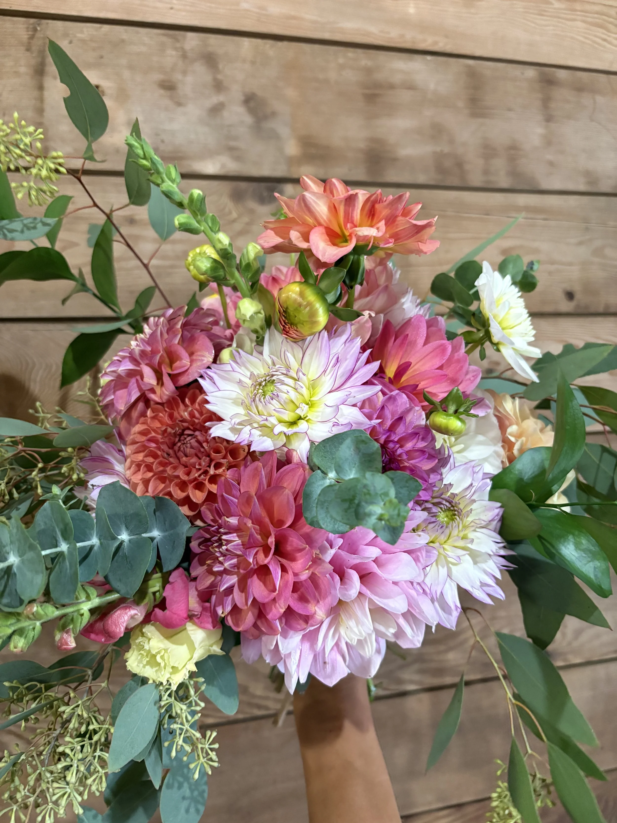 A colorful bouquet of pink, white, peach, and yellow flowers with green foliage against a wooden background.