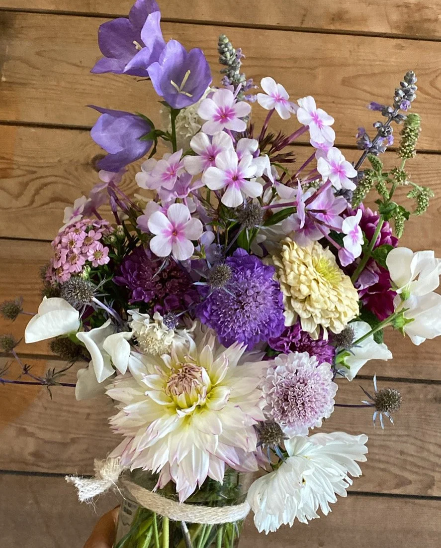 A colorful bouquet of mixed flowers including purple, pink, white, and yellow blossoms against a wooden background.