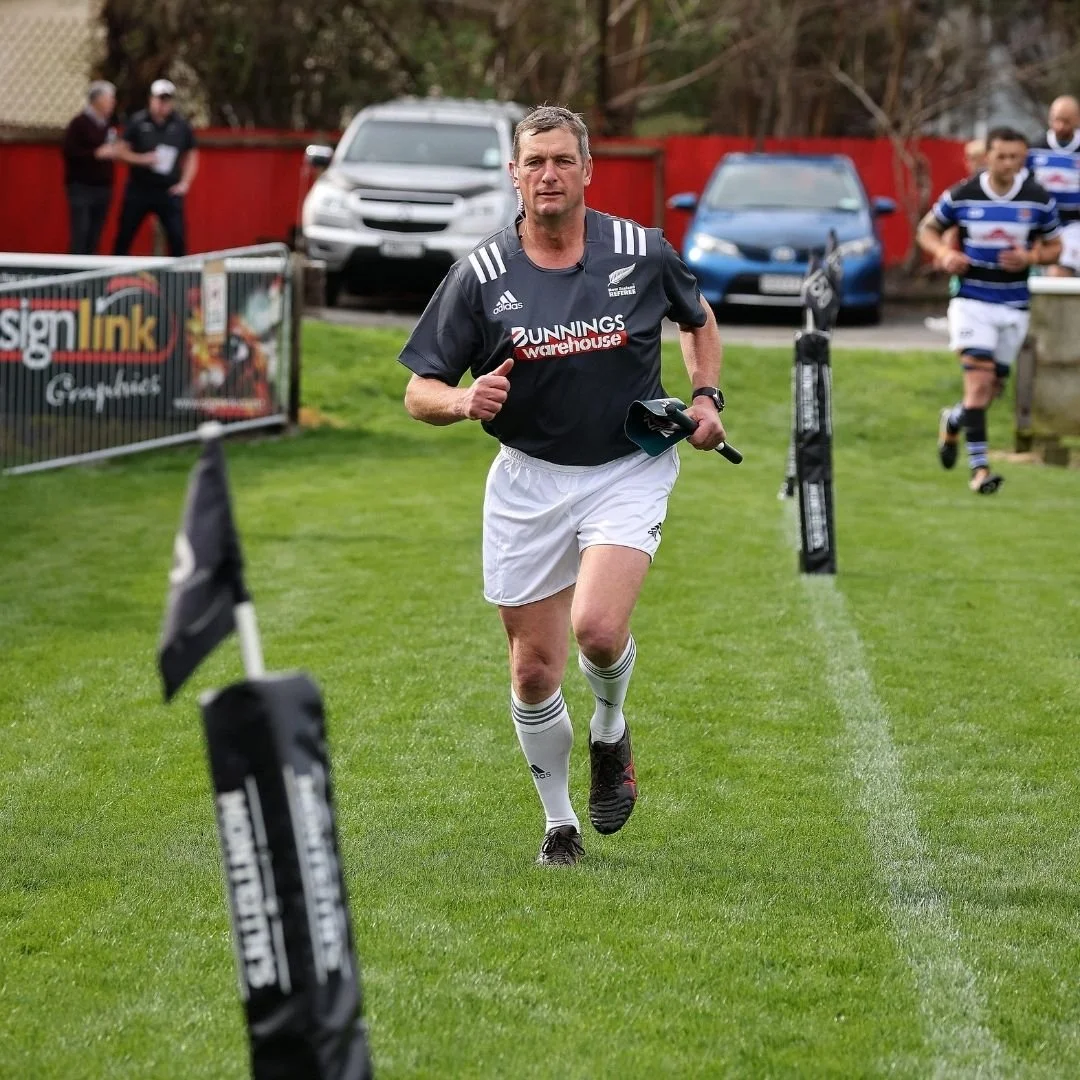 A man in a black rugby jersey and white shorts running on a grassy field during a rugby match or event.