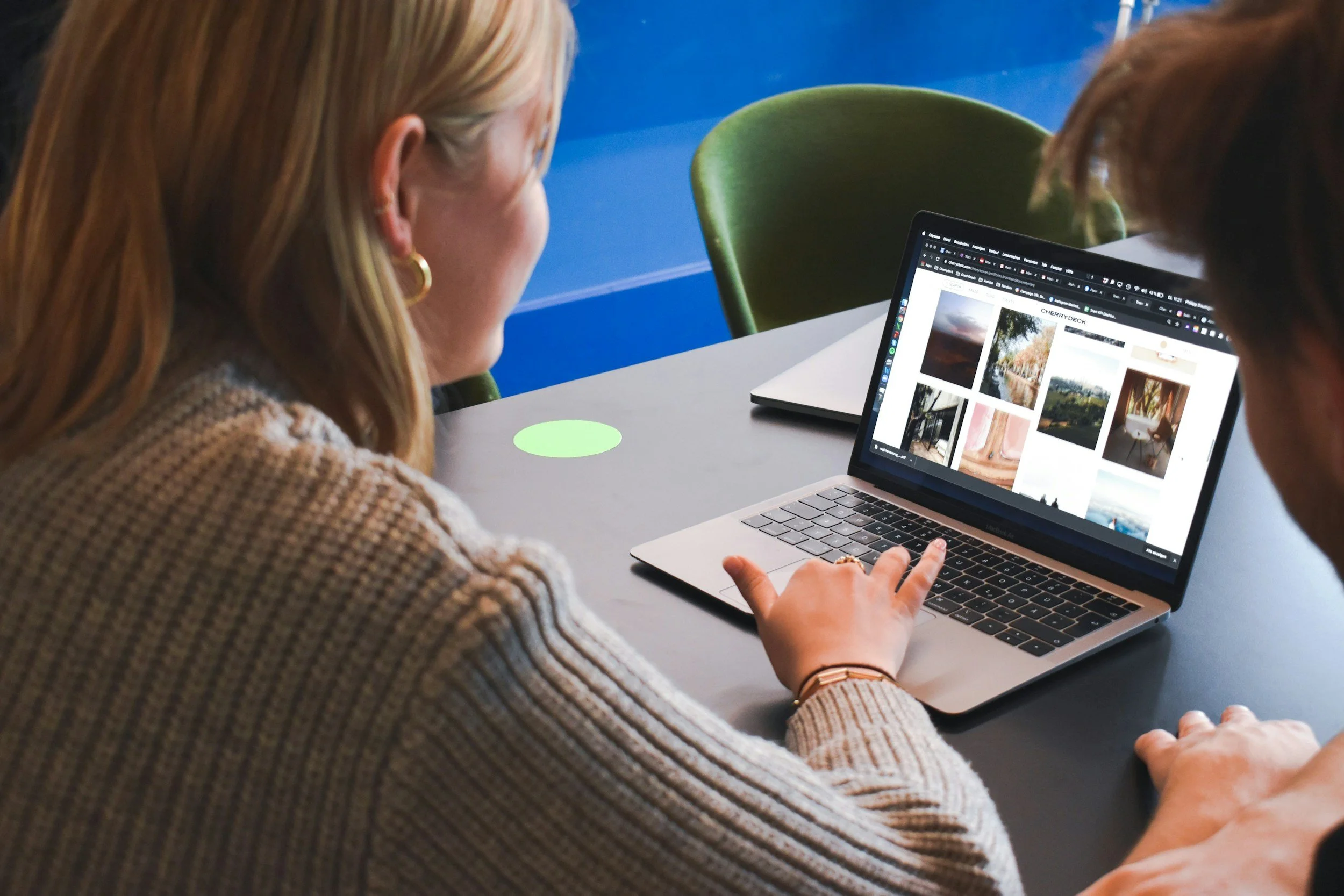 Two women sit at a table looking at a laptop screen working on a website project