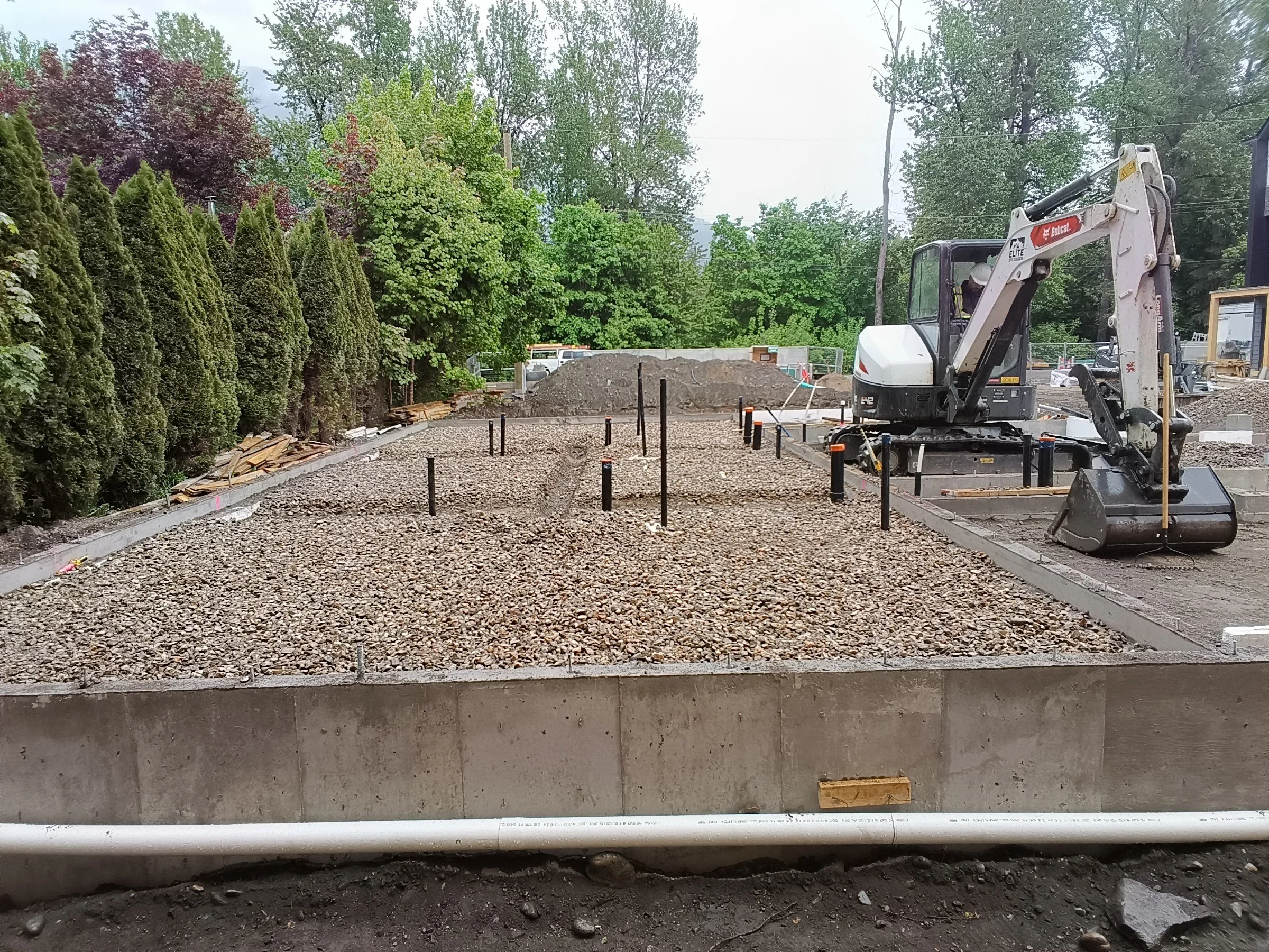 Construction equipment, specifically a yellow road roller, parked next to a dirt embankment in a forested area with tall trees.