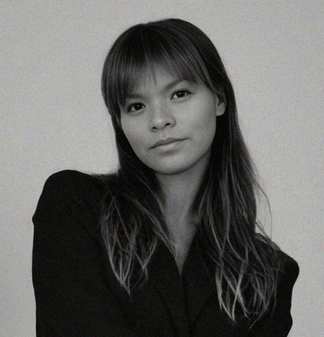 Black and white portrait of a woman with straight hair, wearing a dark blazer, looking at camera with a neutral expression.