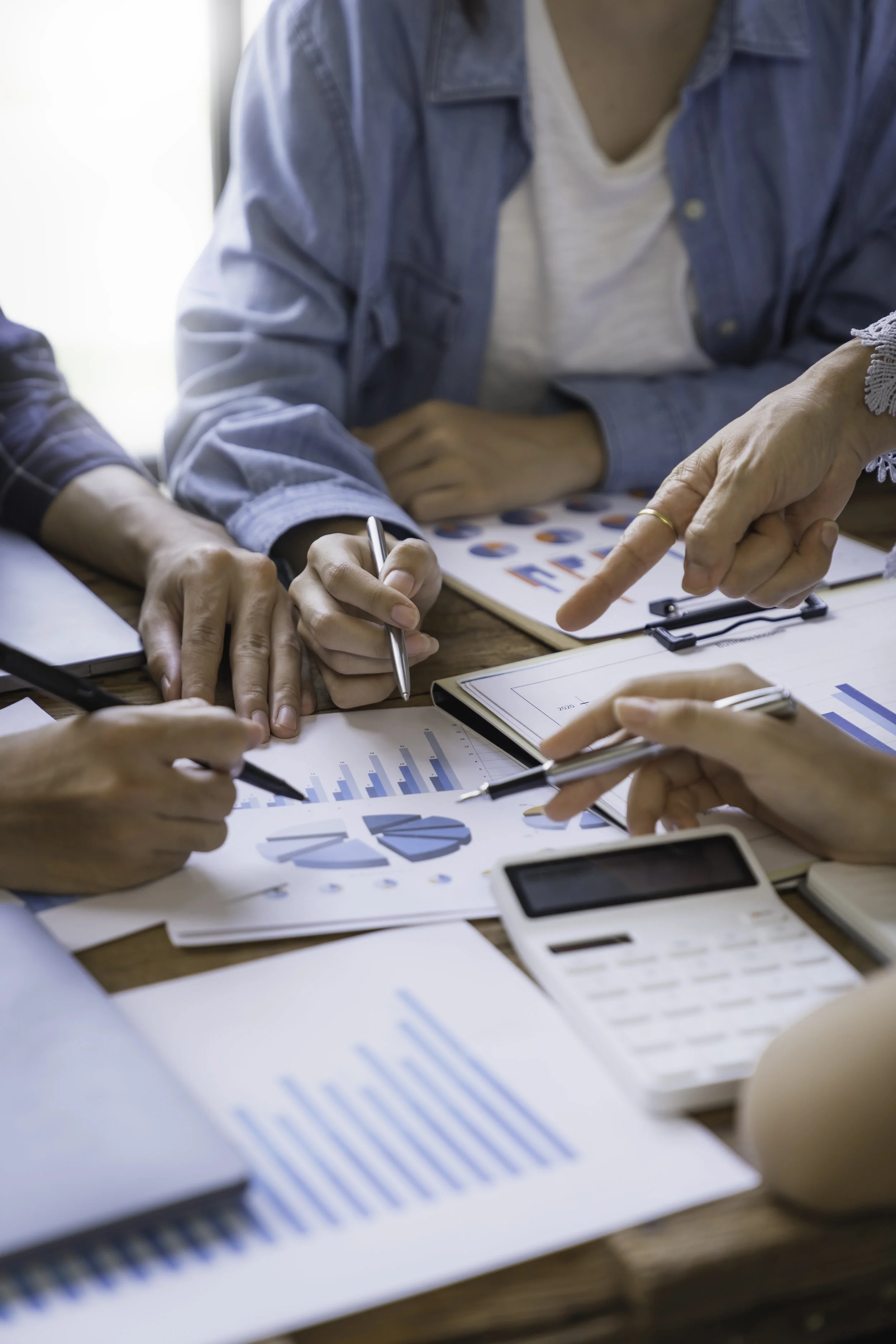People discussing financial data and charts on a wooden table with a calculator, pens, and documents.