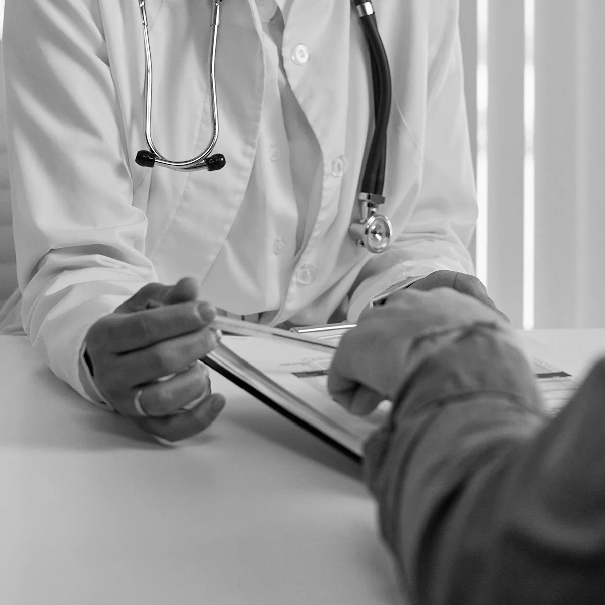 A doctor in a white coat with a stethoscope around their neck is taking notes or filling out a form for a patient.