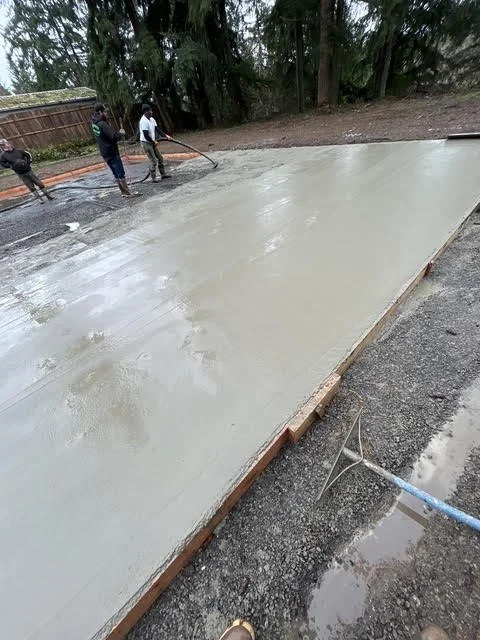 People working on pouring and smoothing a concrete slab in an outdoor area.