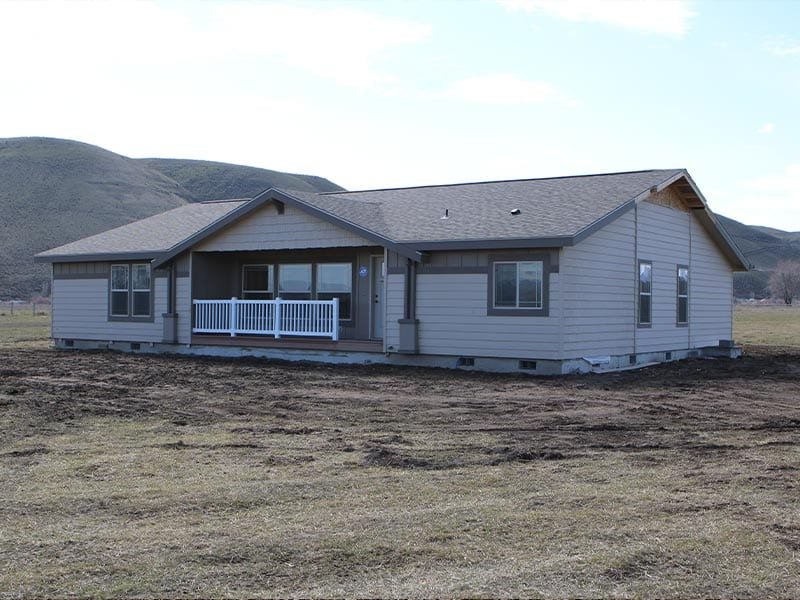 Newly constructed single-story house in a rural area surrounded by hills, with a wooden deck and a white railing in front.
