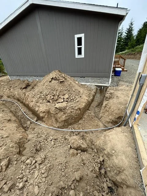 Underground utility work around the foundation of a house with exposed dirt and pipes.