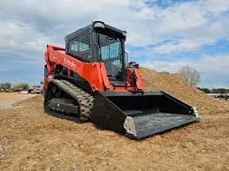 A red compact track loader on a construction site, spreading soil.