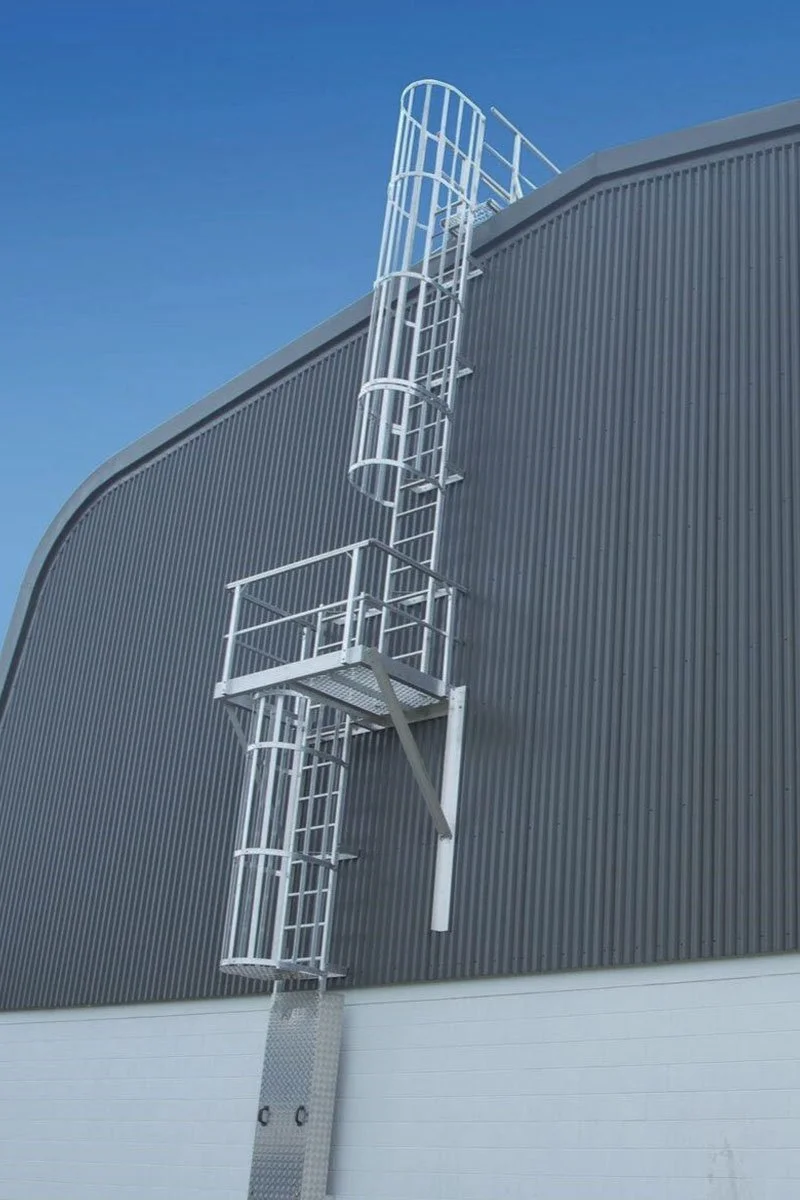 Fixeded ladder access attached to the side of a large building with a corrugated metal exterior and a clear blue sky.